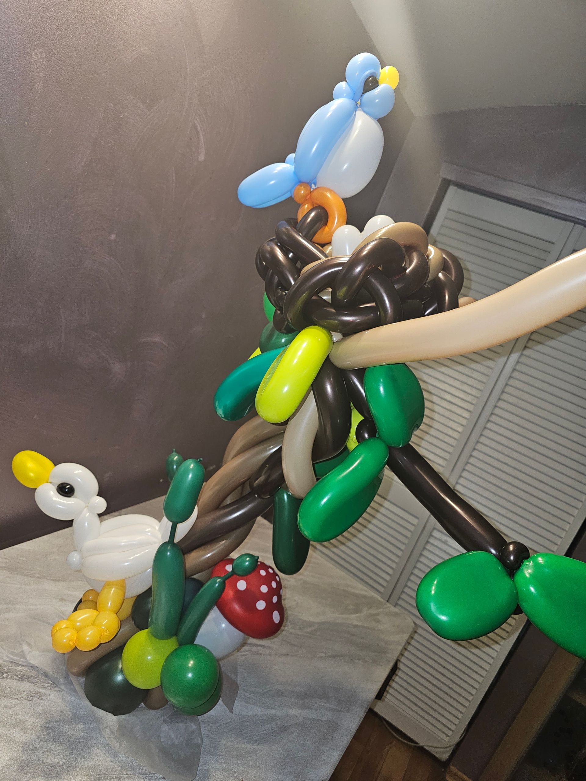 Balloon sculpture of a bird in a nest, featuring a duck, red mushroom, and green leaves.