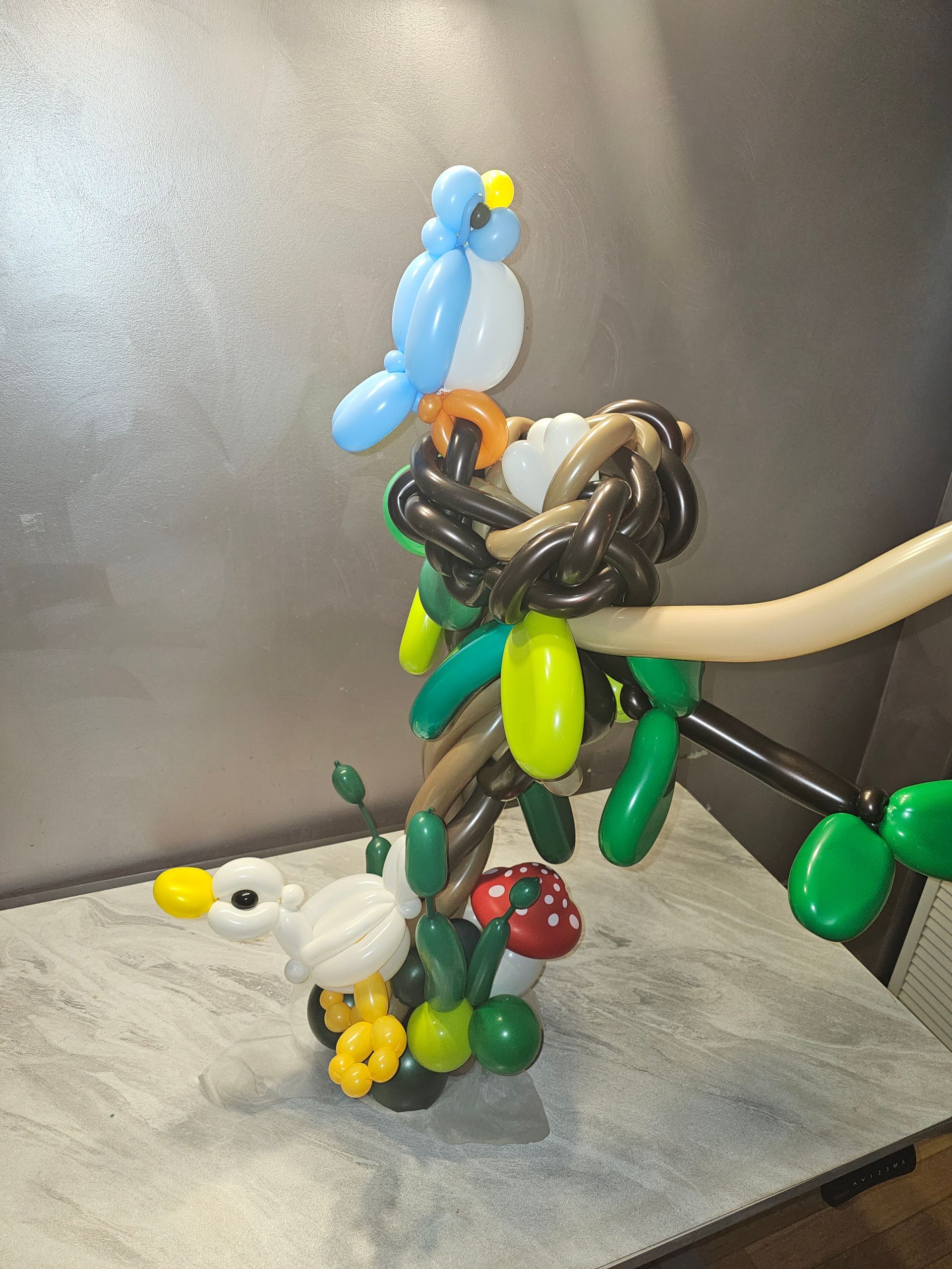 Balloon sculpture of a bird in its nest, with a bluebird and foliage in various colors.