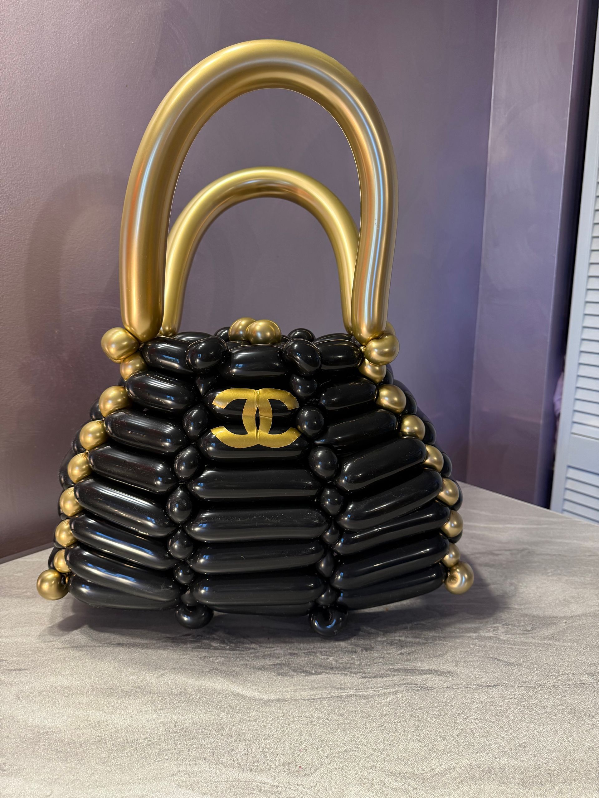 A balloon sculpture of a black handbag with gold handles and logo.