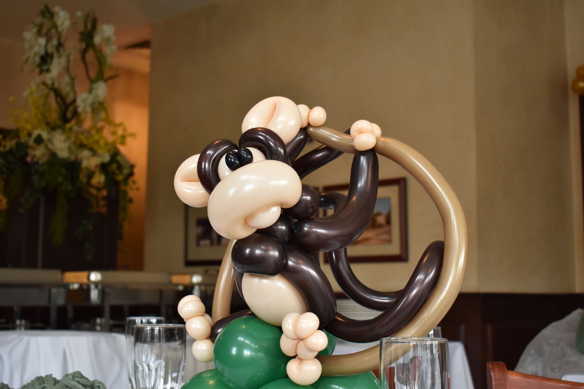 Balloon monkey clinging to a brown ring, on green balloons, indoors.