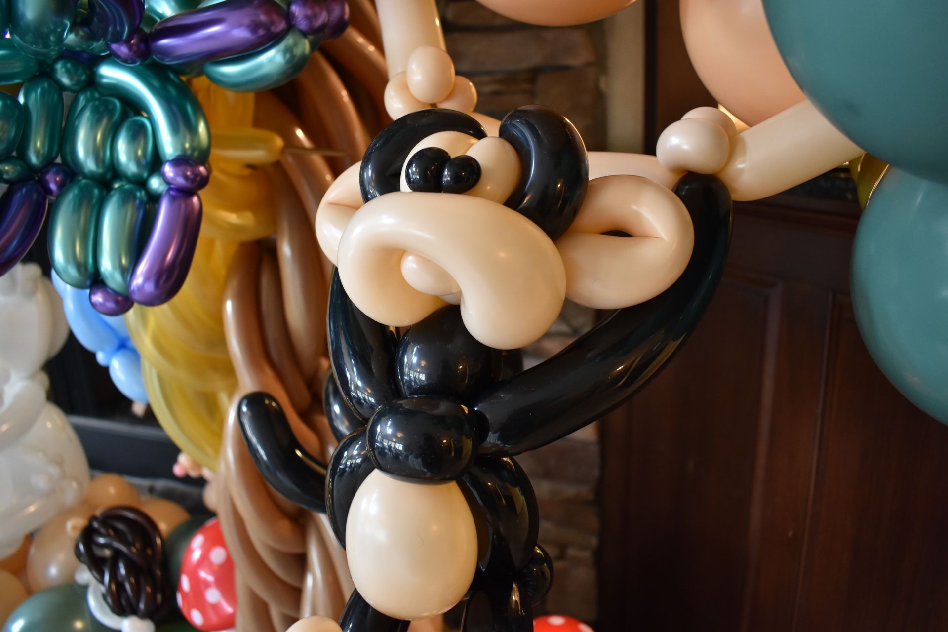 Black balloon monkey sculpture with cream-colored face, arms raised. Part of a larger balloon display.