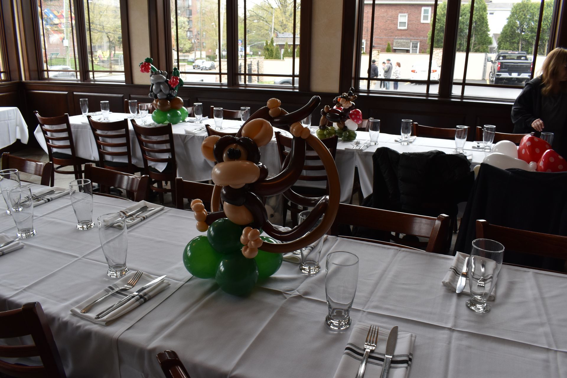 Restaurant table set with monkey balloon centerpiece and glasses, sunlight.