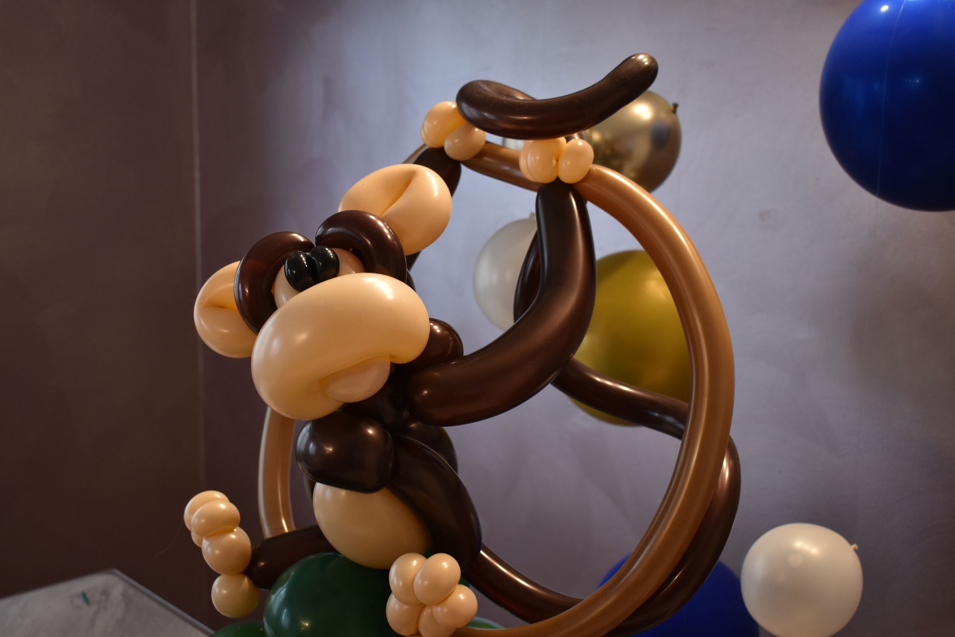 Balloon sculpture of a brown monkey hanging from a brown ring, with tan and green accents.