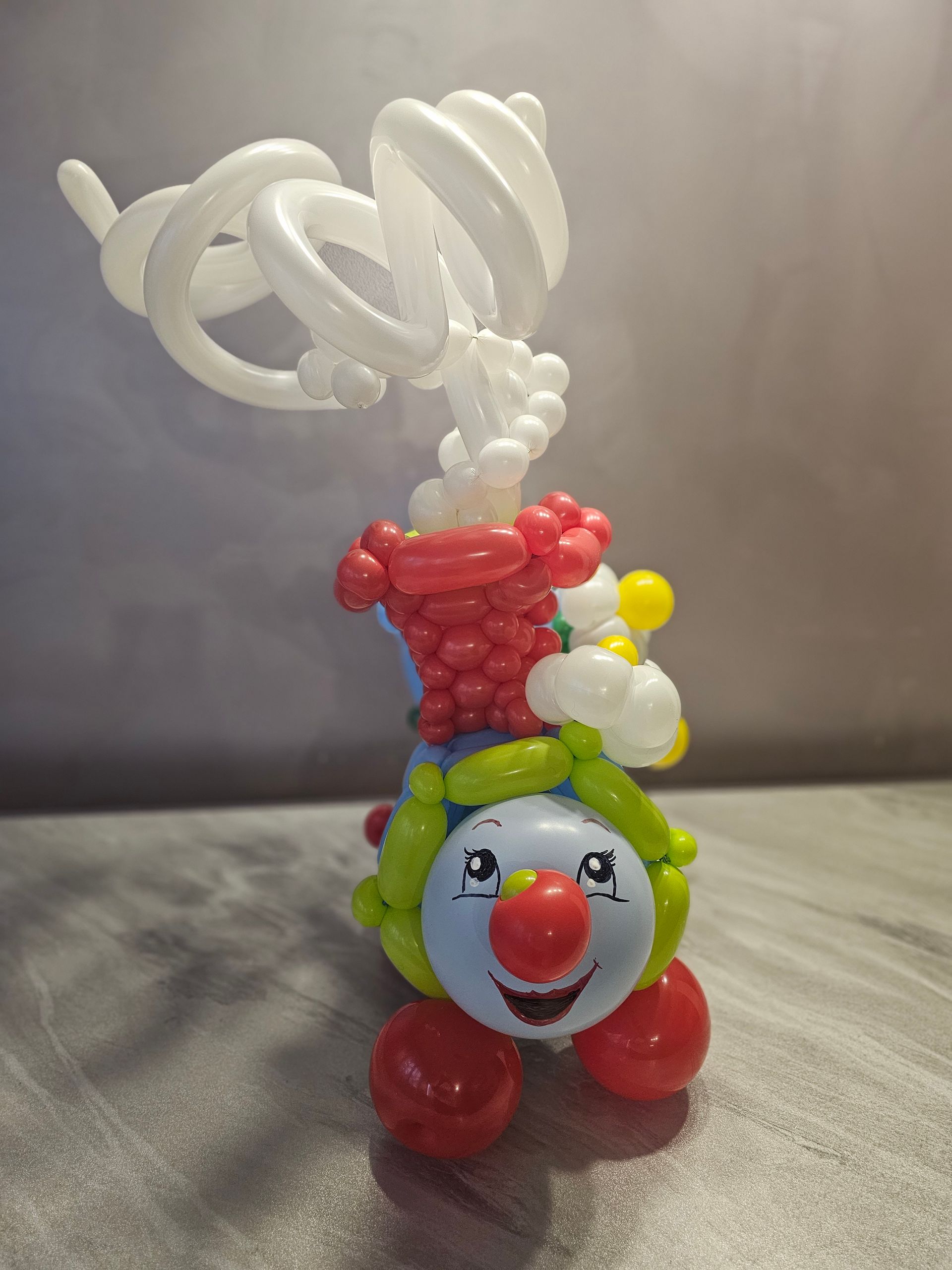 Balloon animal of a smiling blue-faced train with red wheels and a spiraling white chimney on a gray surface.