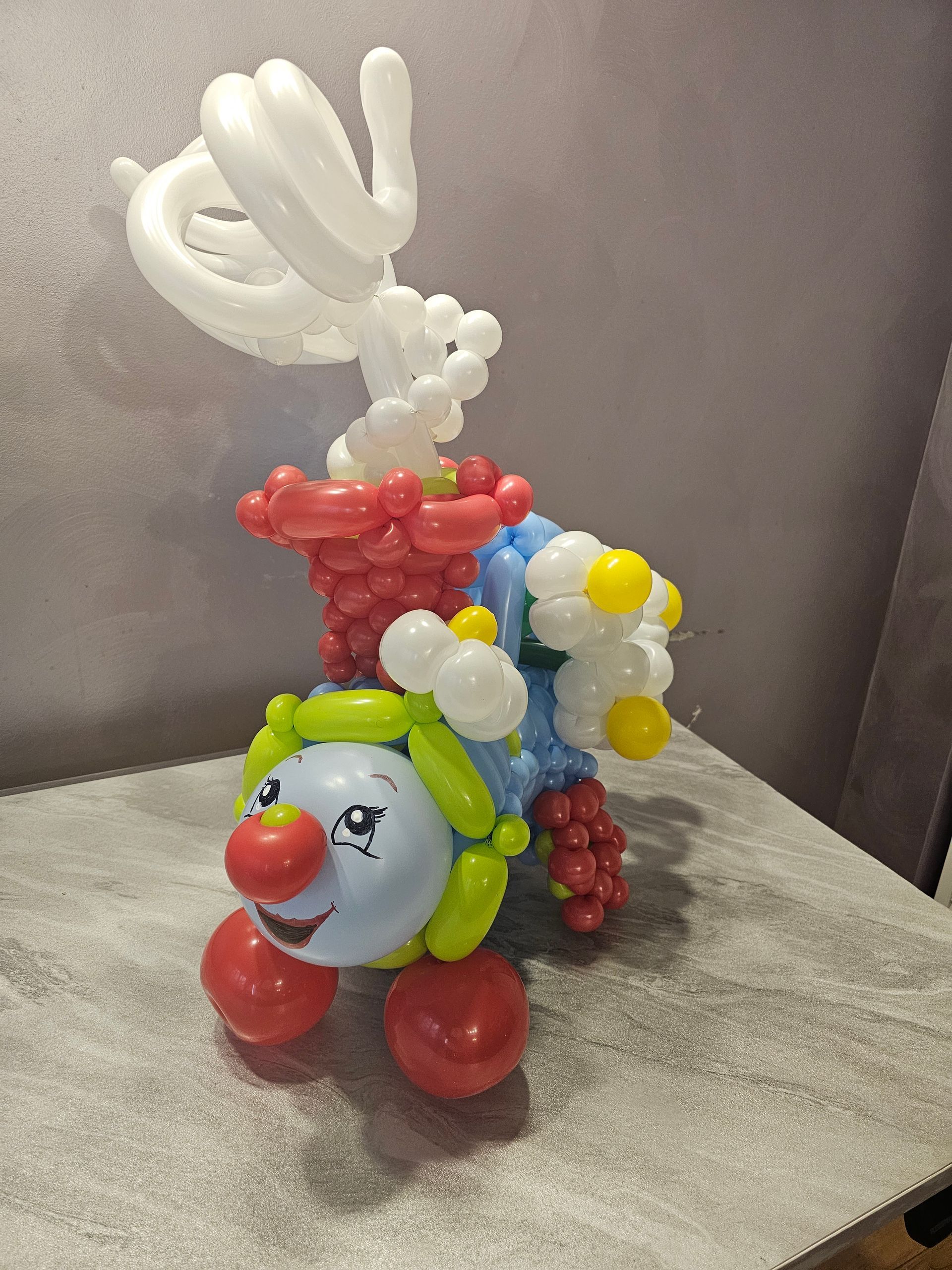 Balloon animal sculpture of a clown riding a decorated vehicle; red, white, yellow, and blue balloons.