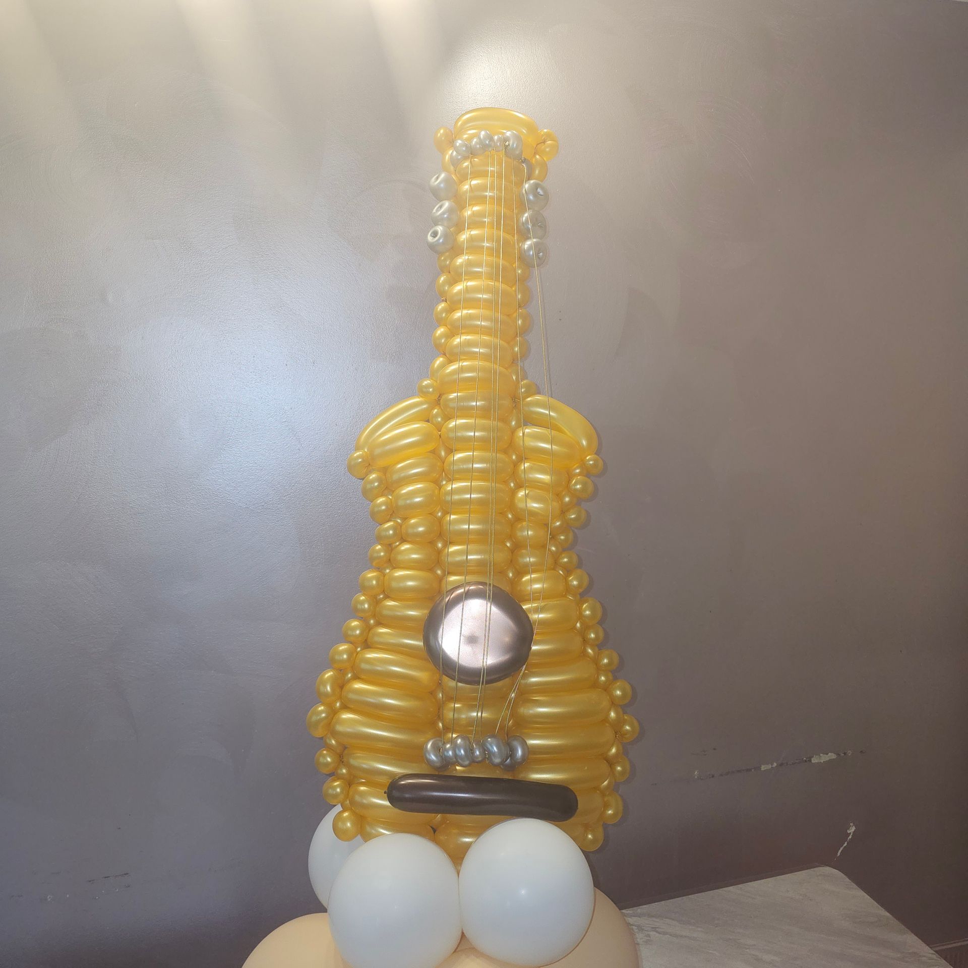 Yellow balloon guitar sculpture with white and cream-colored balloon base.