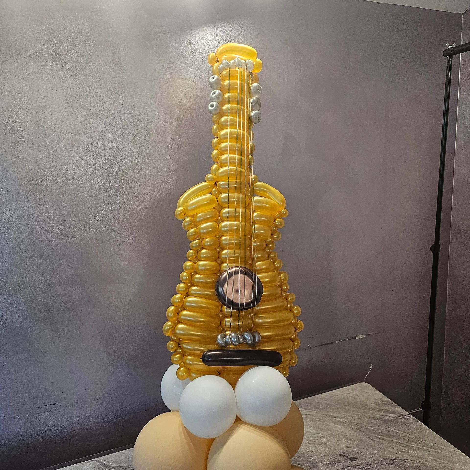 Golden balloon ukulele sculpture on a base of balloons, against a gray background.