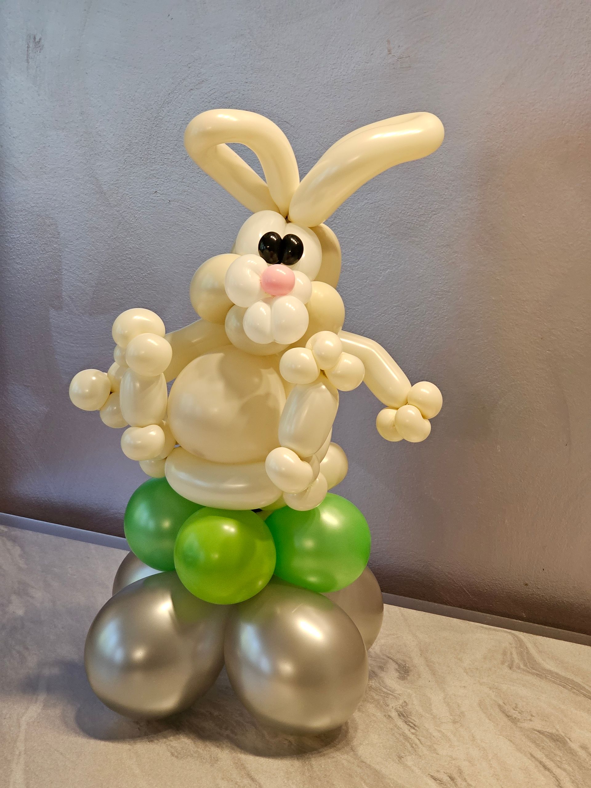 Balloon sculpture of a cream-colored bunny with green and silver base; standing.