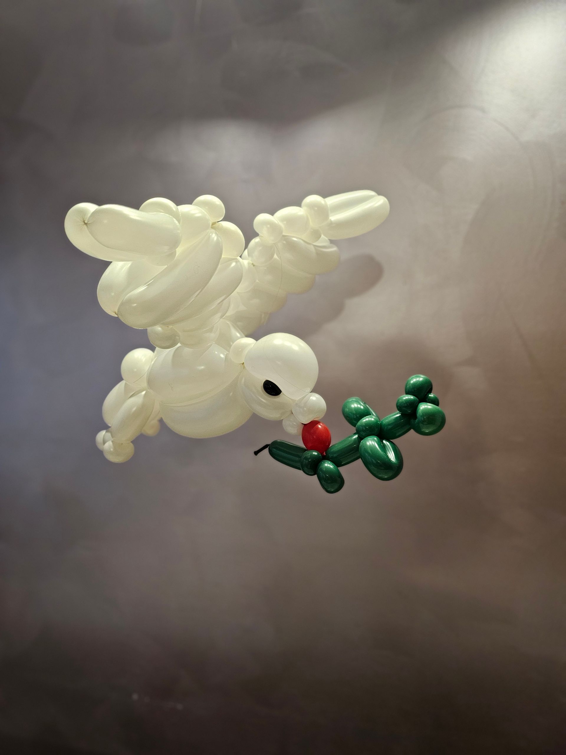 Balloon sculpture of a white angel carrying a green balloon branch with a red balloon berry.