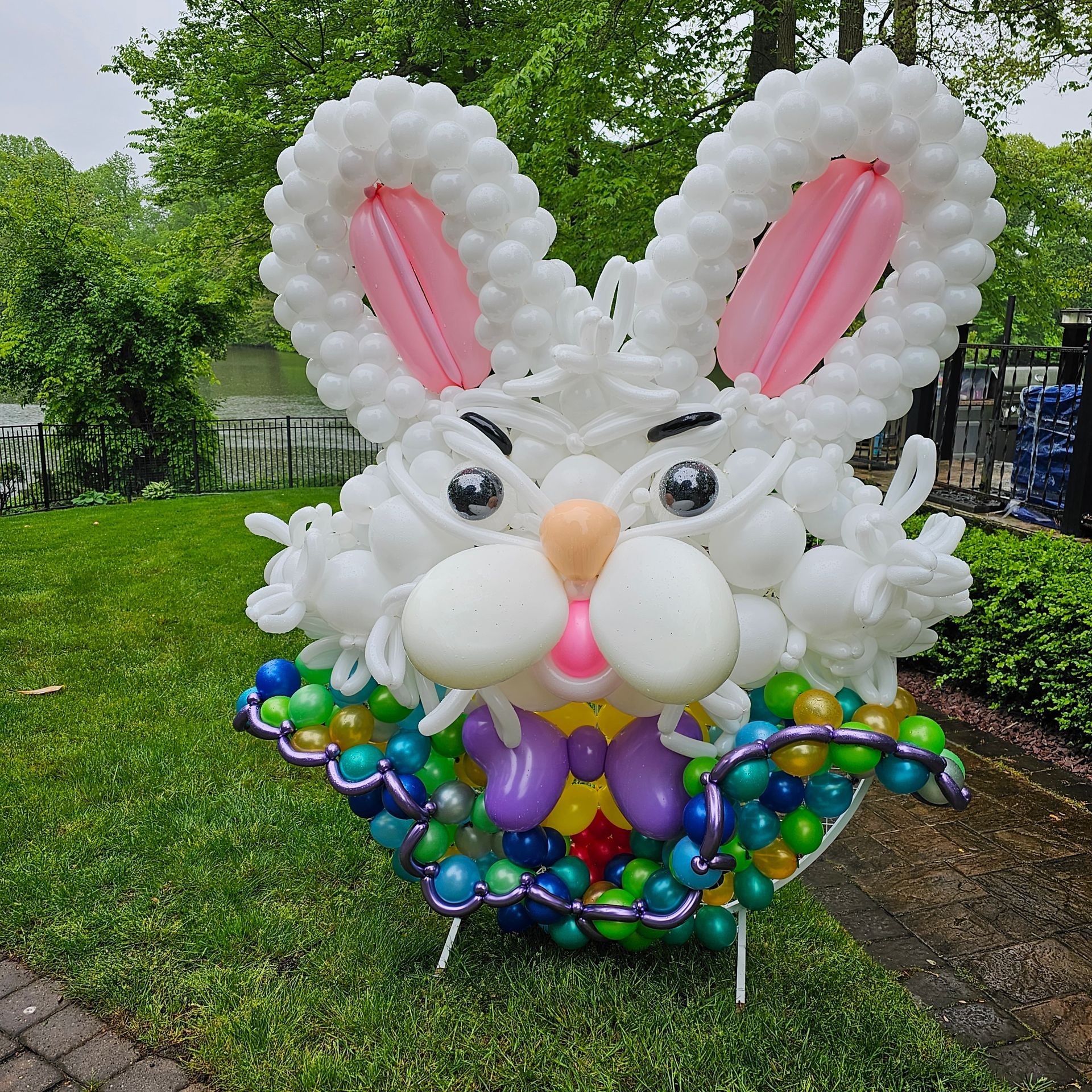A whimsical Easter bunny sculpture made of white and colorful balloons sits on green grass.