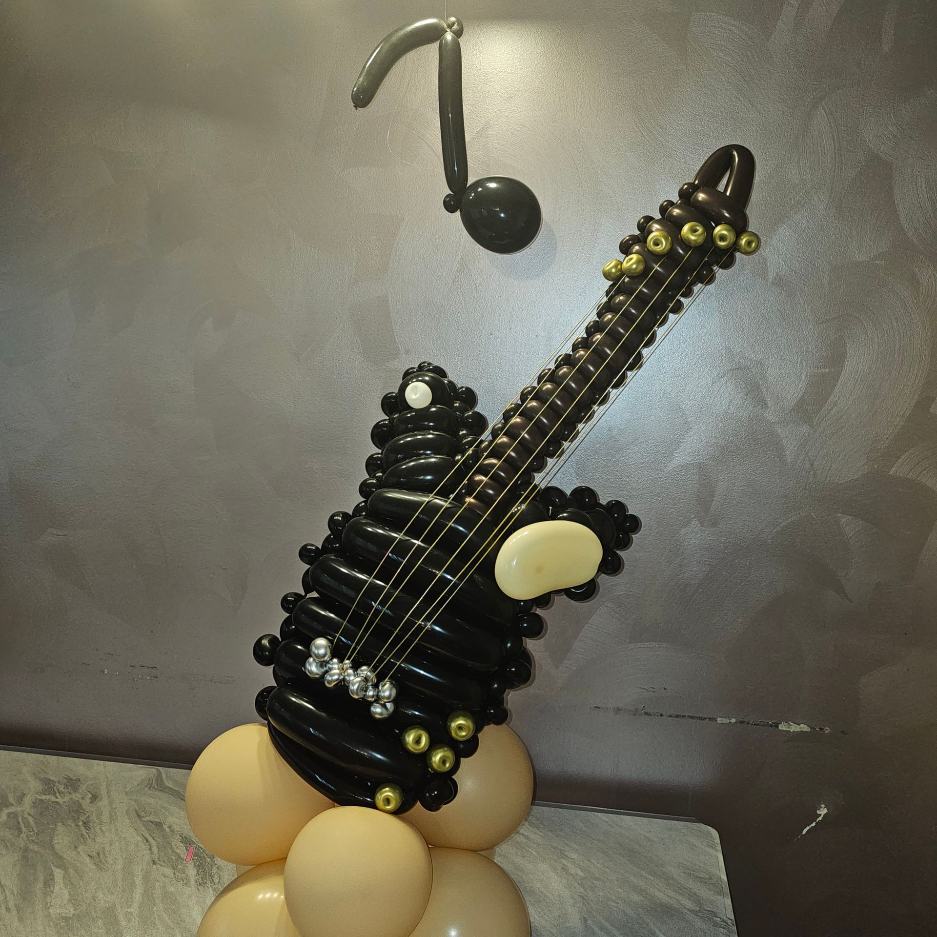 Black balloon guitar sculpture with a musical note, beige balloons at the base.