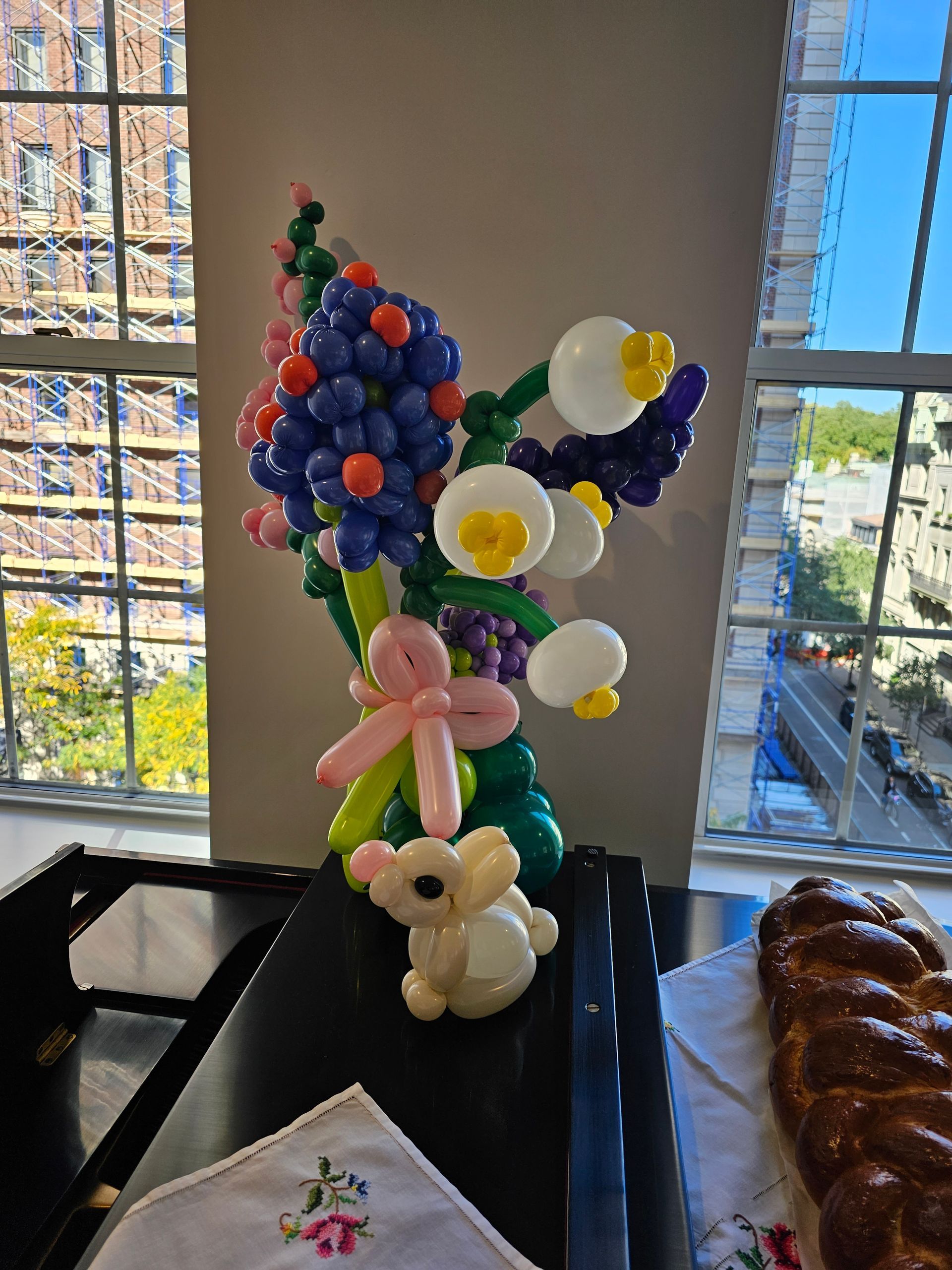Balloon bouquet with Easter bunny and braided bread on a table near a window.
