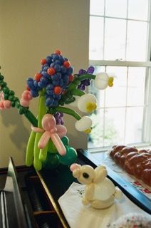 Balloon flowers, including blue, white, and pink, on a table near a window and food.