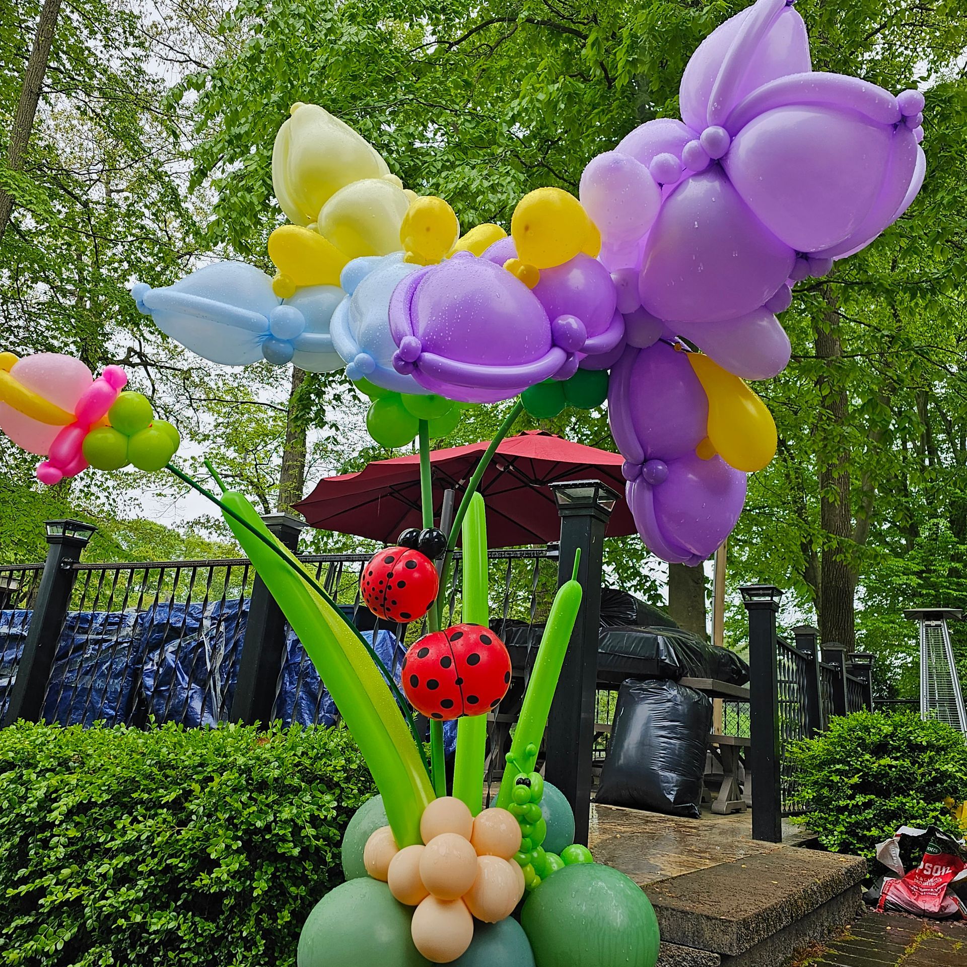 Balloon flower arrangement with ladybugs, green stems, and colorful petals, outdoors.