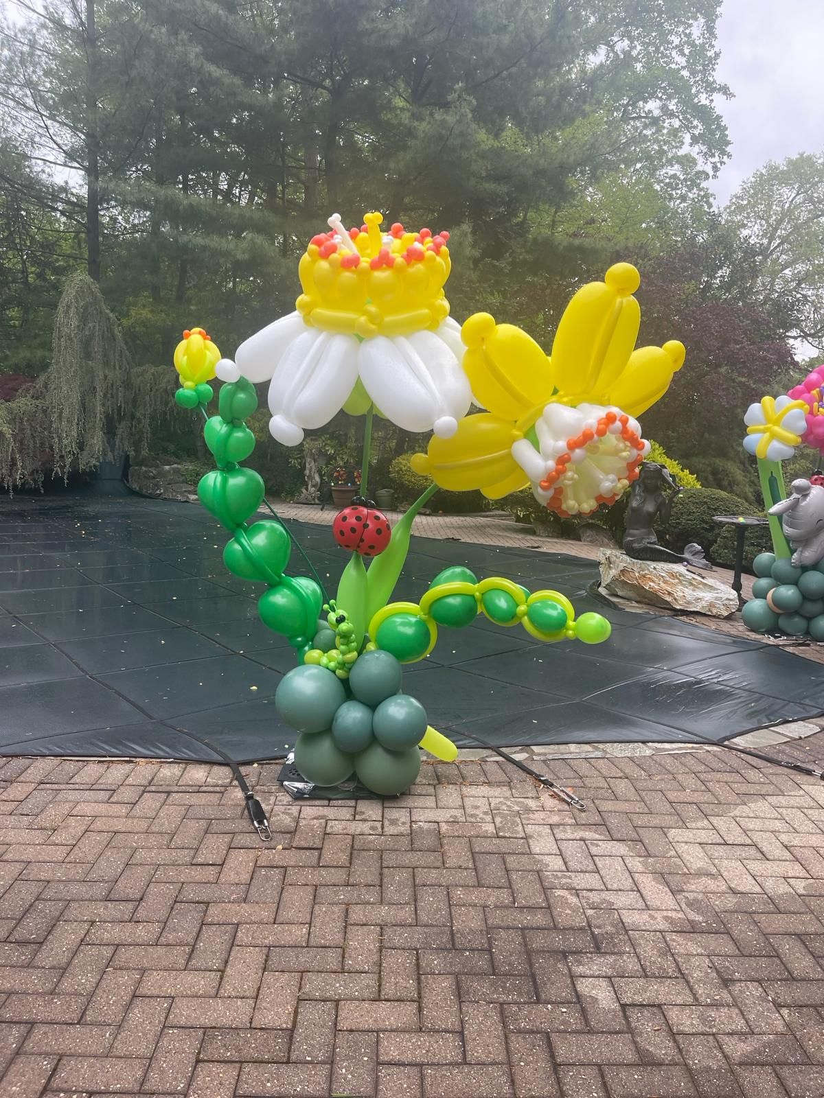 Balloon sculpture of daffodils and a ladybug on a patio near a pool.