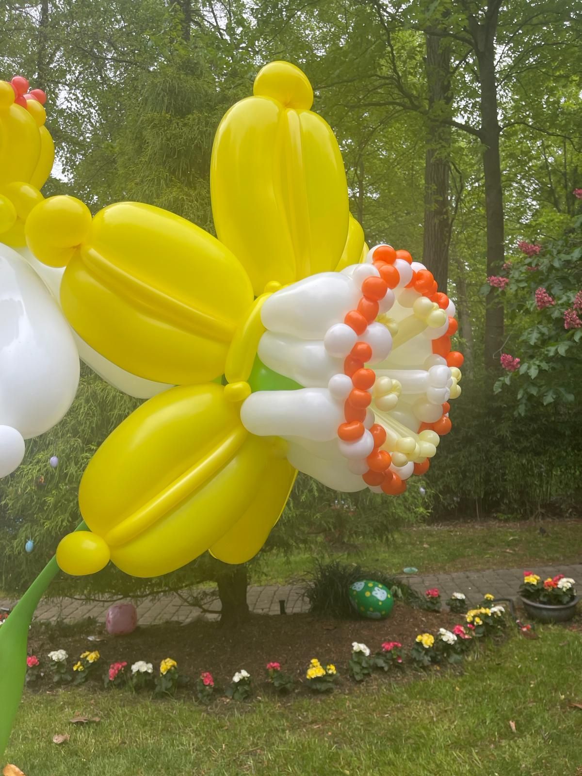 Yellow and white daffodil sculpture made from balloons in a garden setting.
