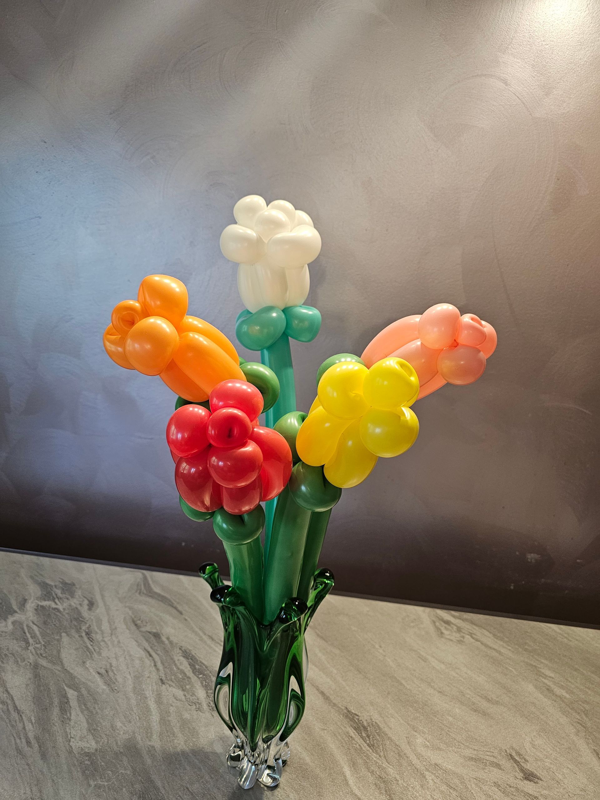 Colorful balloon flowers in a green glass vase against a gray and textured background.