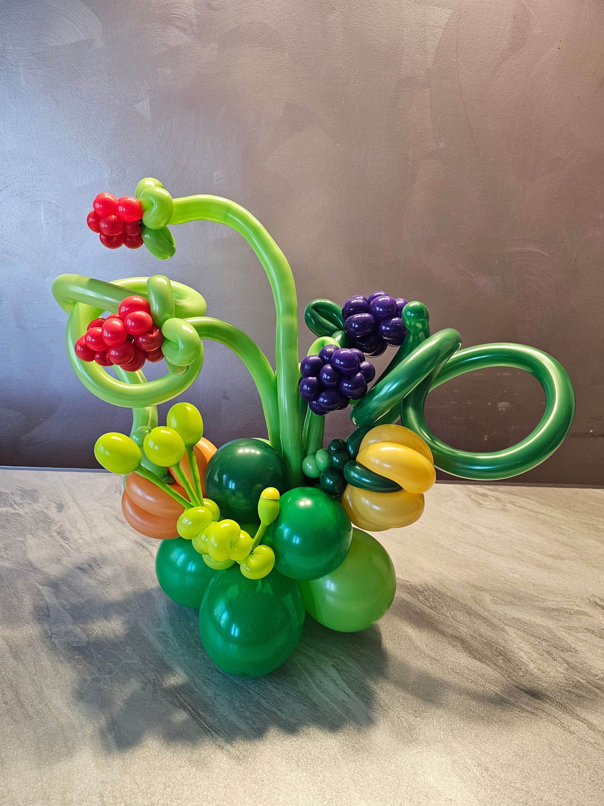 Balloon sculpture of fruit in various colors: red, purple, yellow, and green.