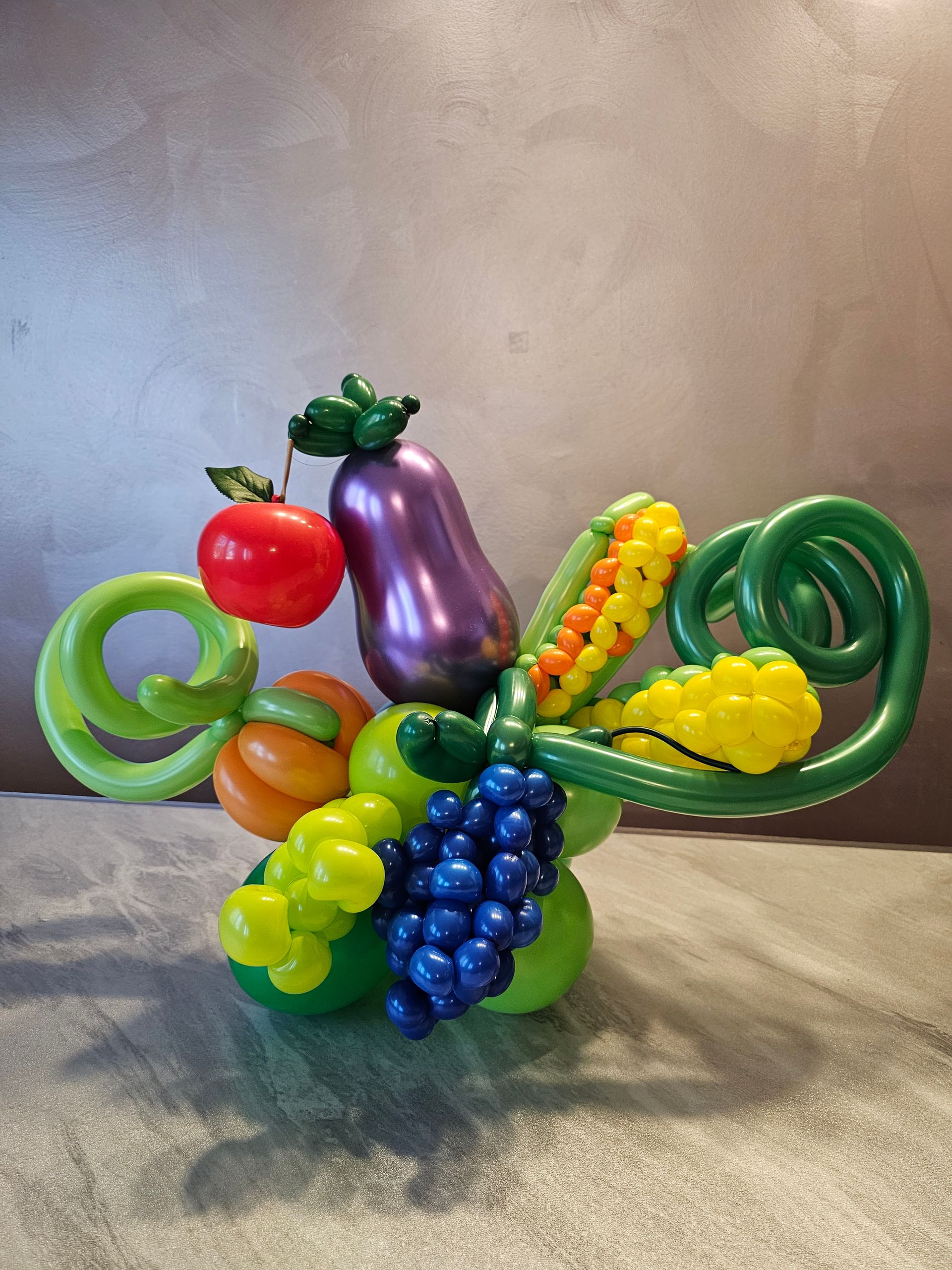 Balloon sculpture of various fruits and vegetables in green, red, yellow, purple, and orange.