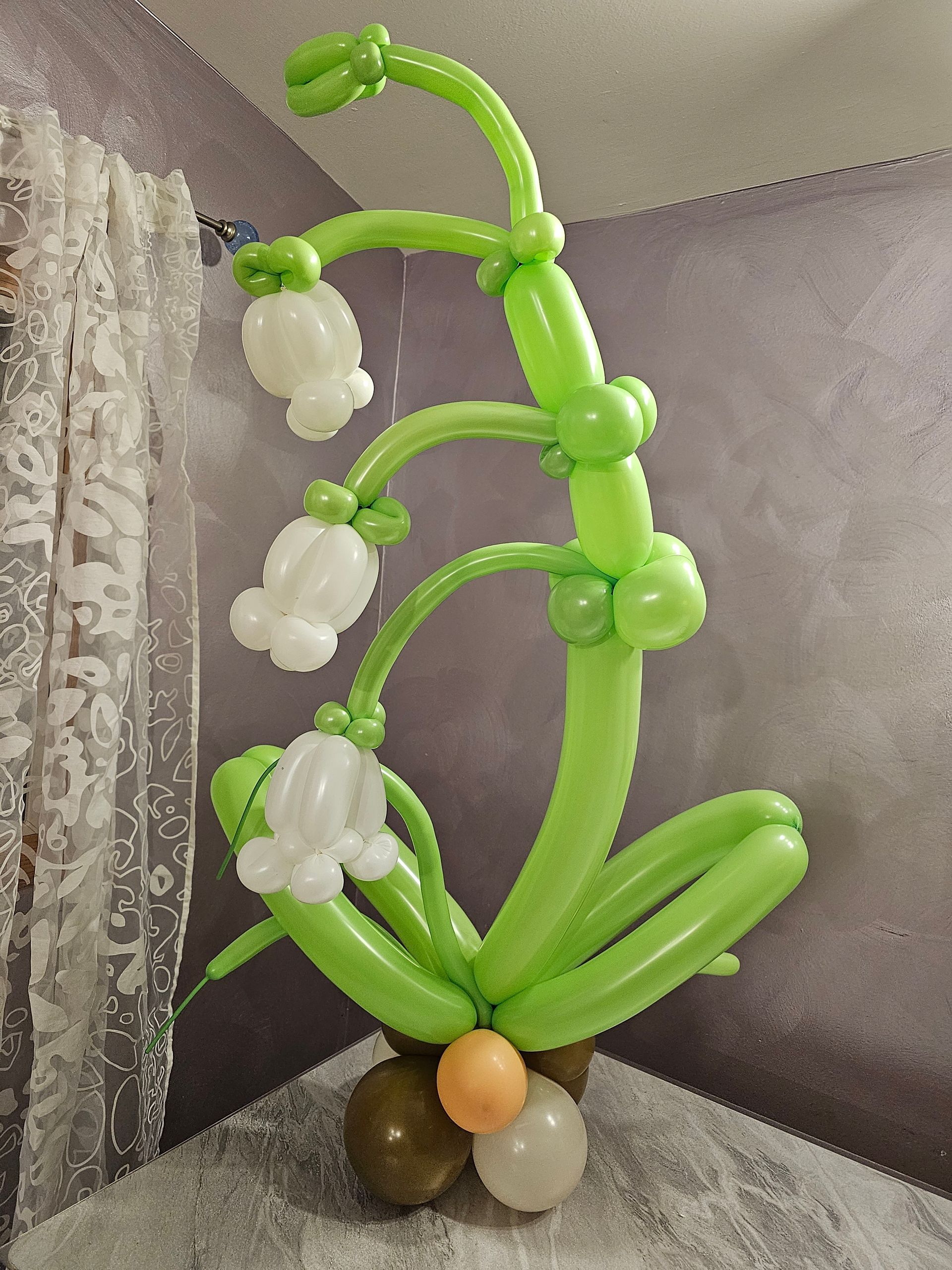 Balloon sculpture of lily of the valley flowers: green stems, white bell-shaped flowers, brown and beige base.