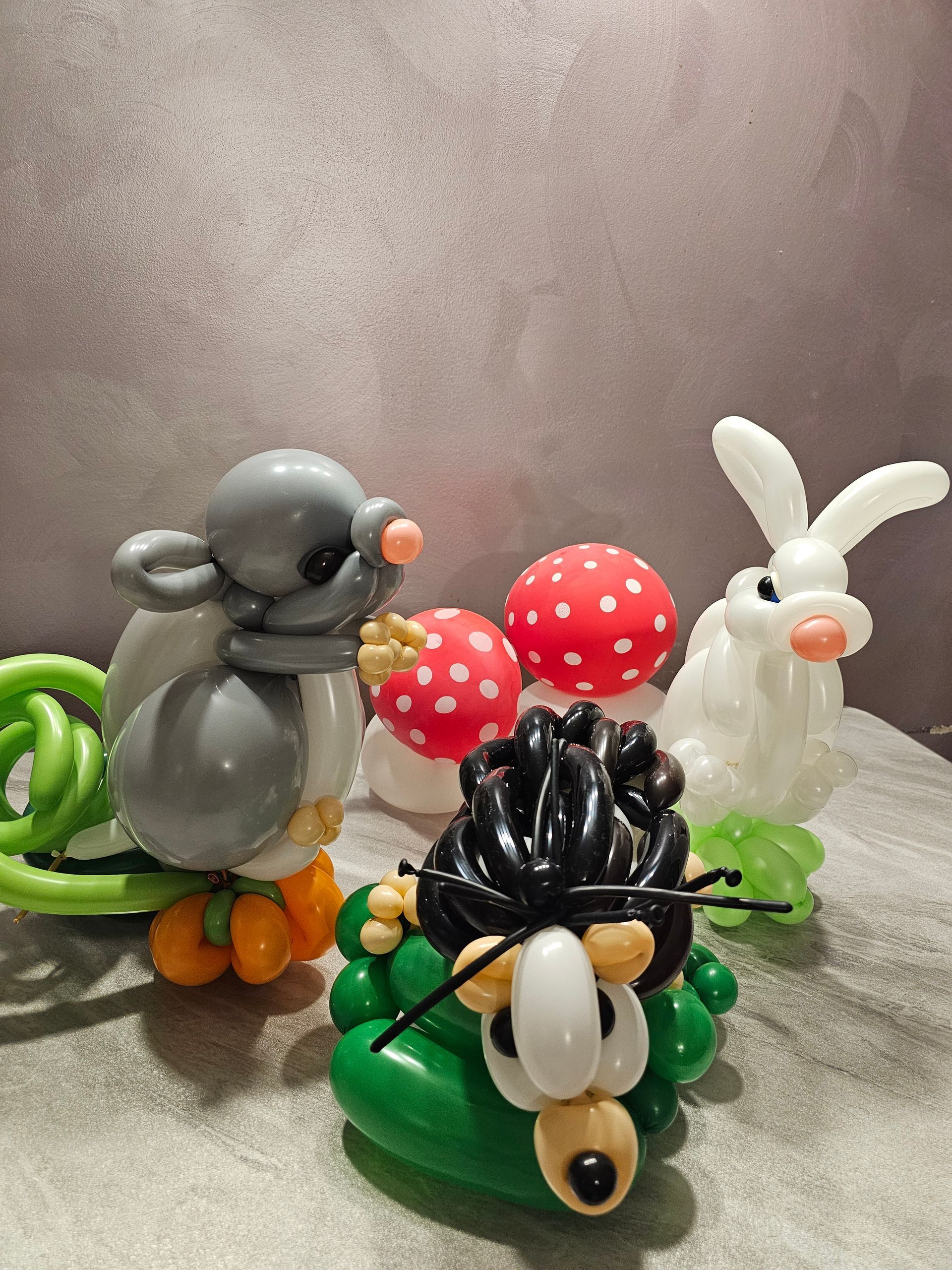 Balloon animals: mouse, rabbit, lion, and mushrooms, set on a surface against a textured gray background.