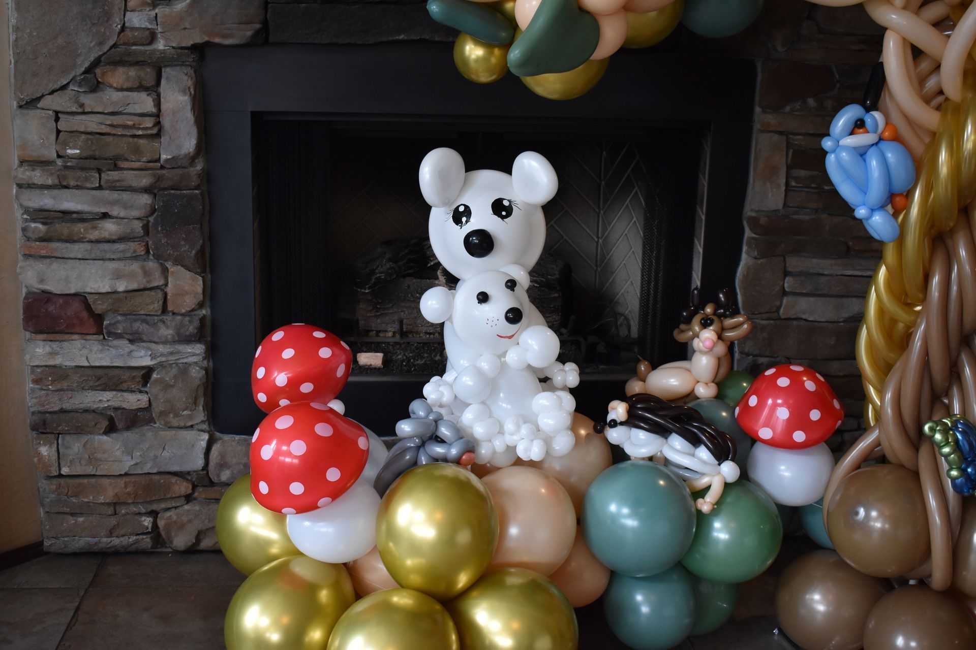 Balloon animals, including mice, deer, mushrooms, and a bird, are set in front of a fireplace.