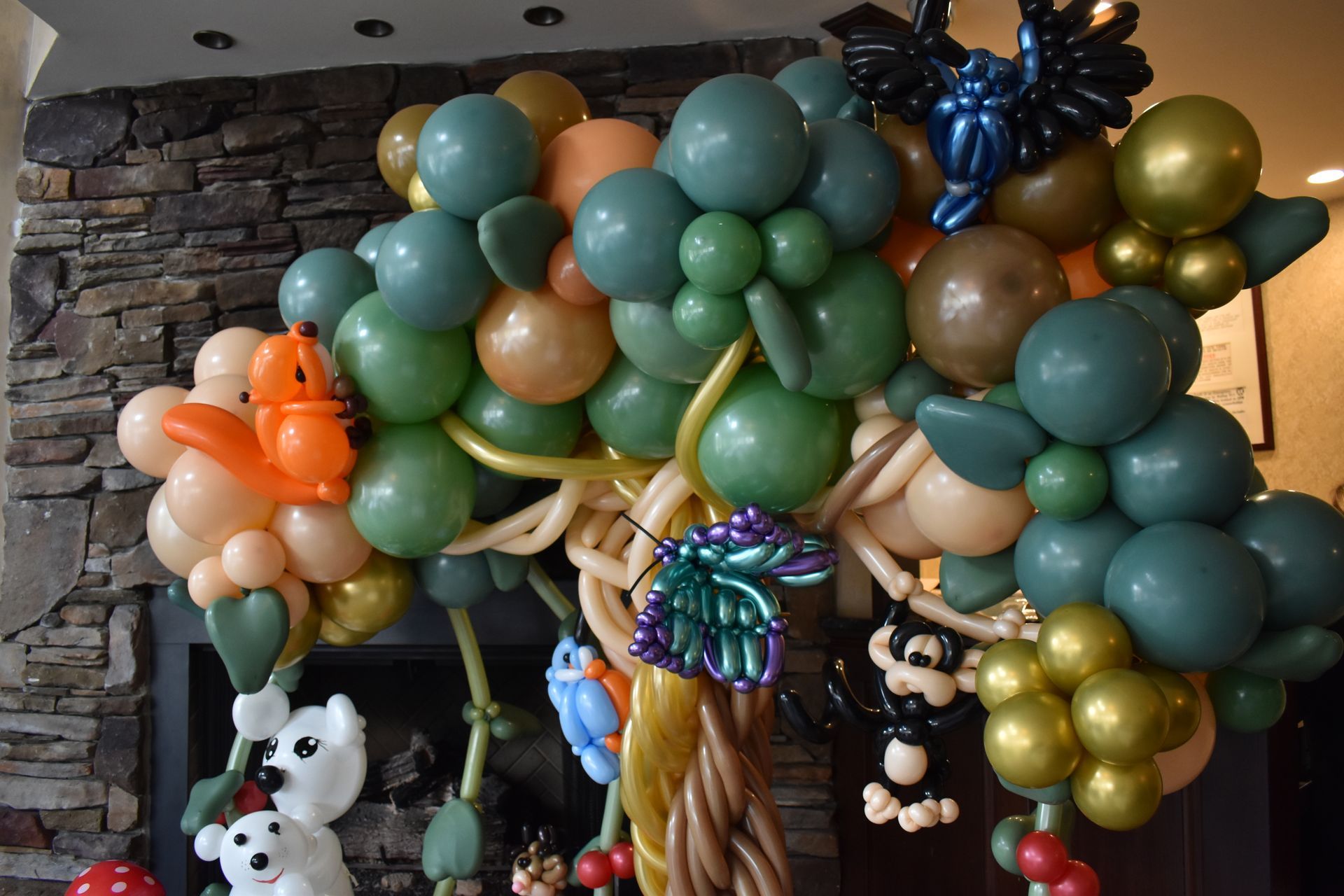 Balloon sculpture of a tree with various animals and colorful balloons, set against a stone wall.