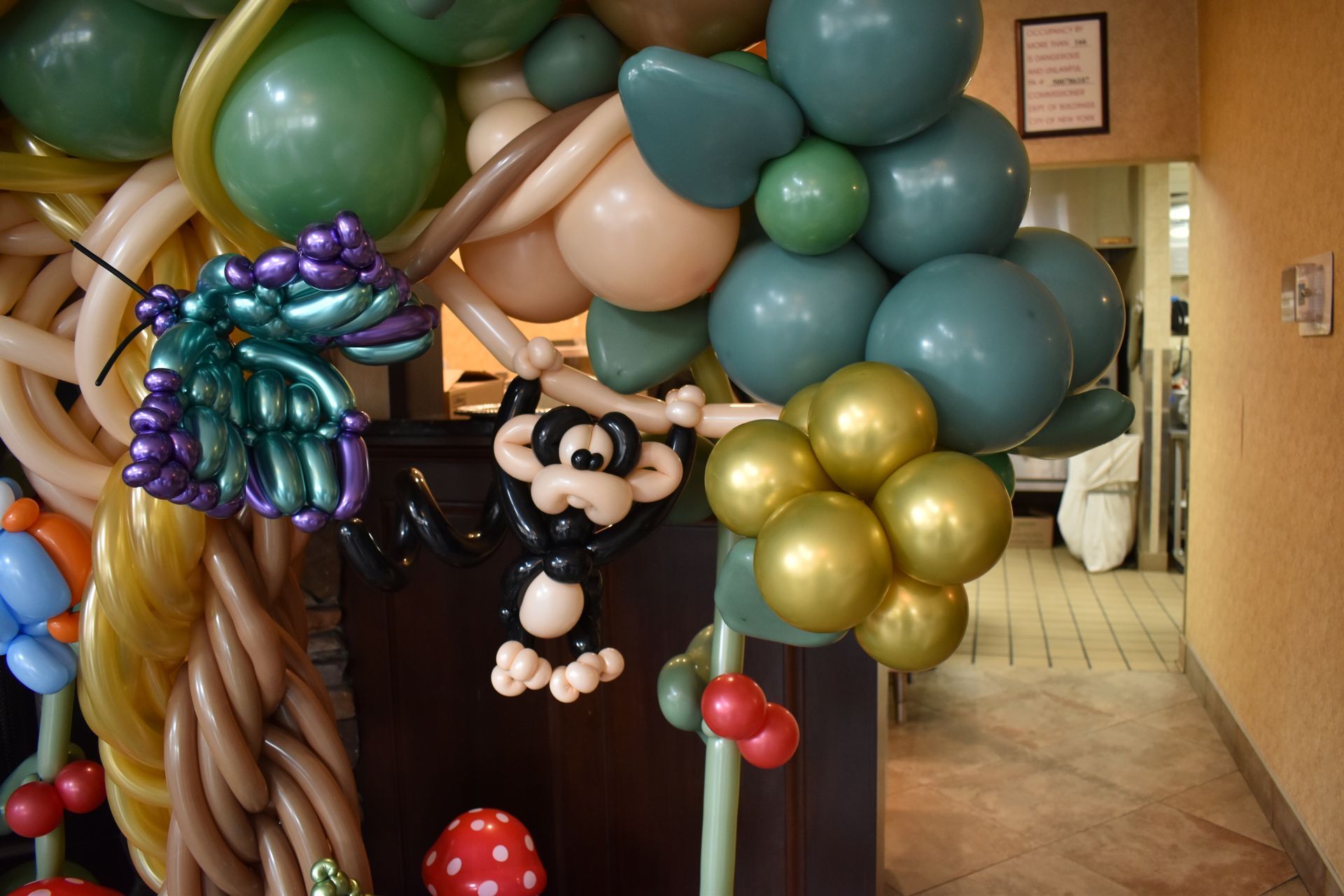 Balloon sculpture featuring a black and white cartoon character hanging from green balloons, with a purple butterfly.