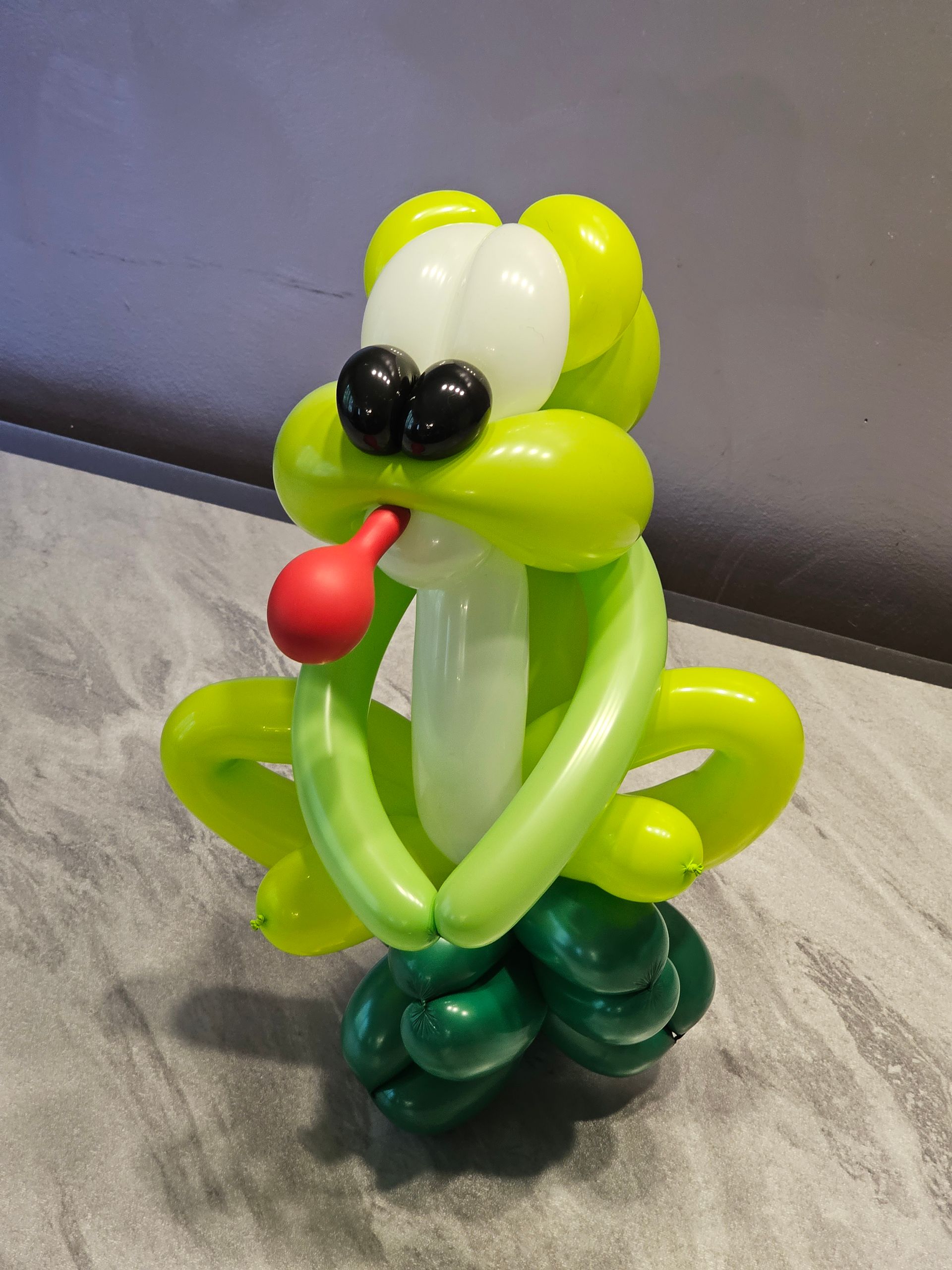 Green balloon animal of a frog with a red tongue, black eyes, and white and green balloons.