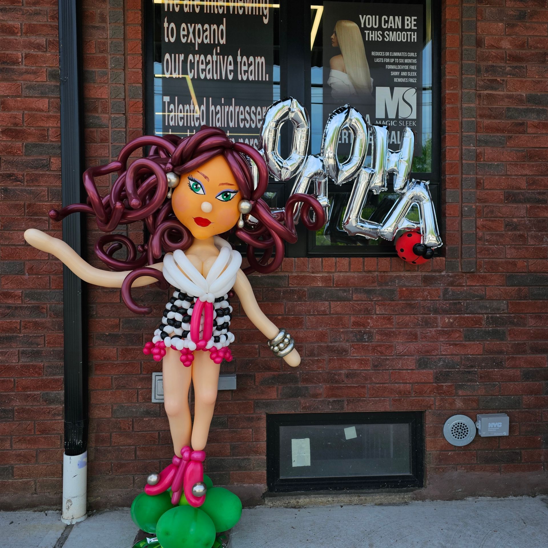 Balloon figure of a woman, with curly hair and fashionable outfit, outside a storefront.