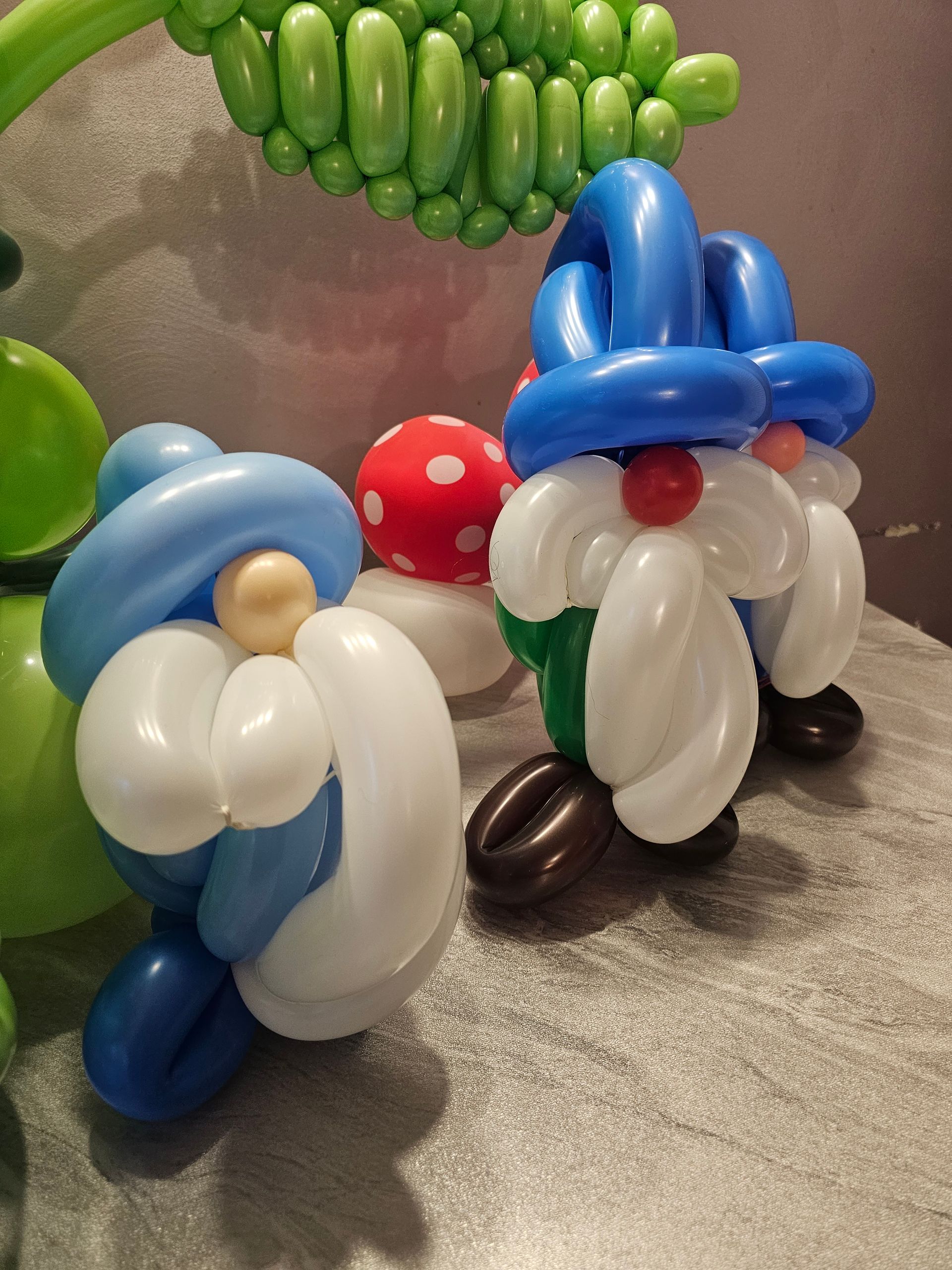 Balloon sculptures of two gnomes with blue hats, white beards, and a red mushroom.