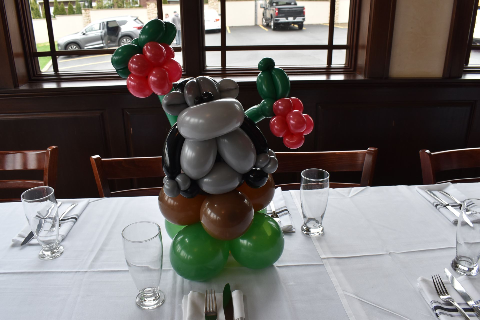 A balloon sculpture of a cow on a decorated table; green, red, brown, and grey balloons.