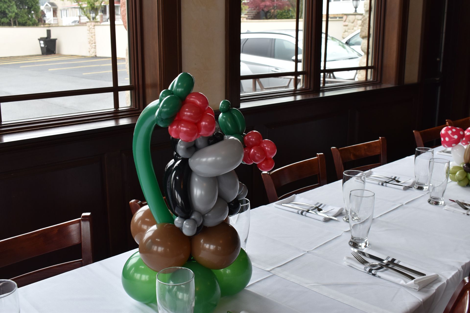 Balloon animal centerpiece on a table set for dining, green, brown, grey, and red balloons.