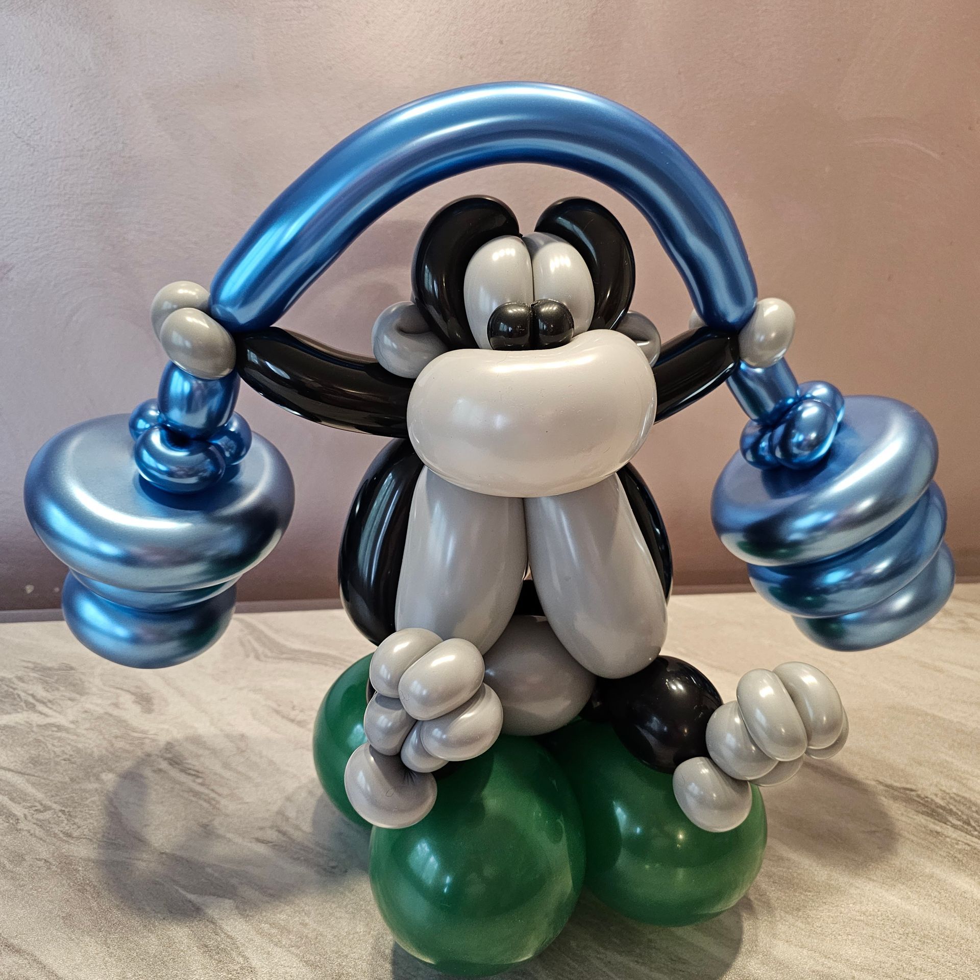Balloon sculpture of a cartoon monkey wearing blue headphones and holding blue weights.