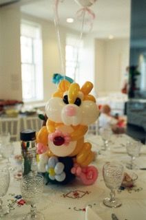 Balloon sculpture of an orange and white bunny with flower embellishments on a decorated table.