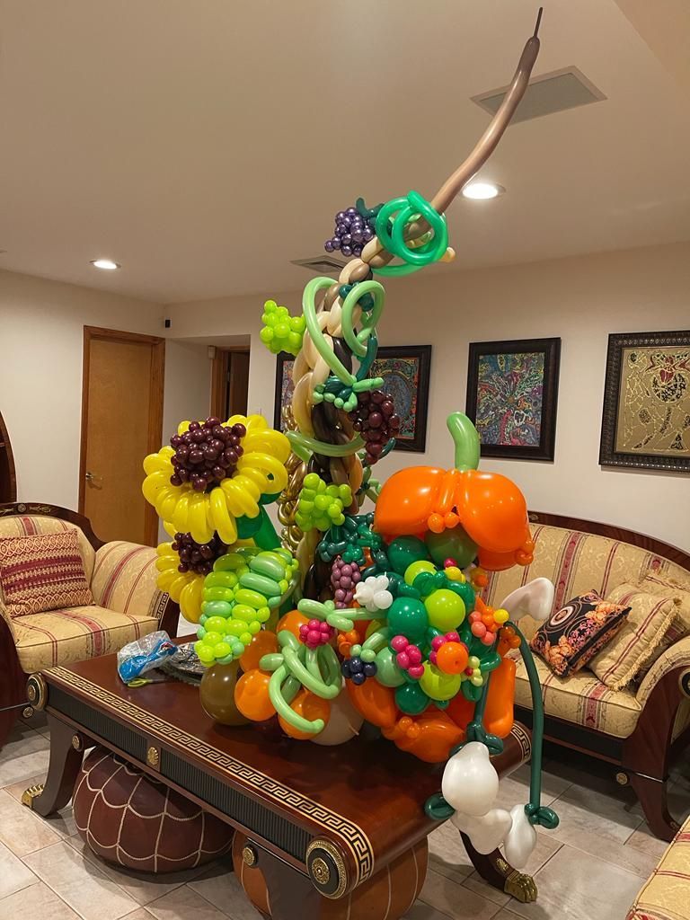 Balloon art centerpiece on a table, featuring a sunflower, pumpkin, grapes, and other floral elements.