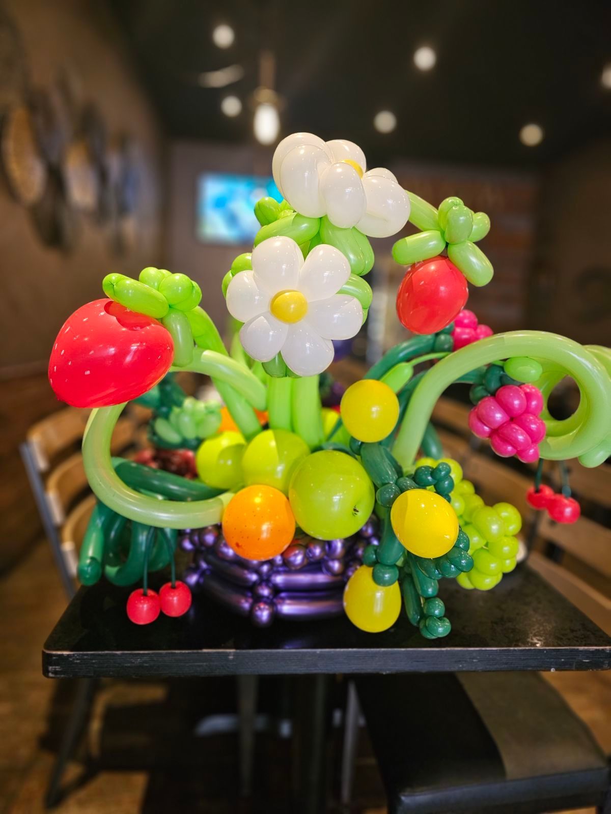 Balloon sculpture of a fruit basket with colorful flowers, including strawberries, grapes, and citrus fruit.