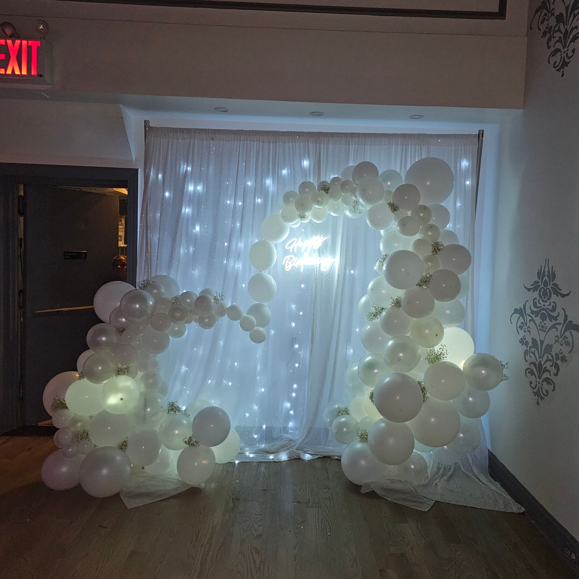 White balloon arches frame a twinkling curtain backdrop, near a doorway.