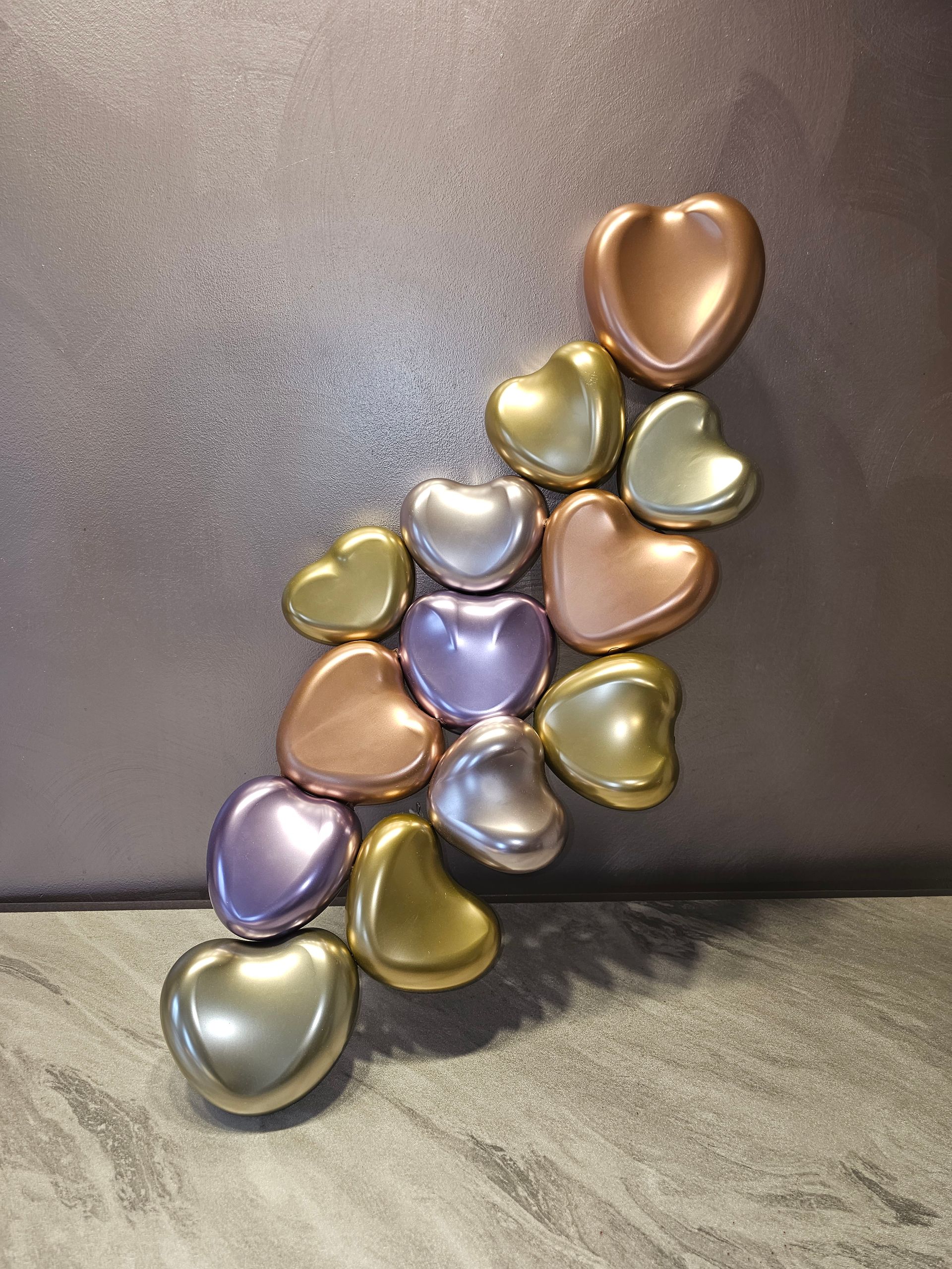 Metallic heart-shaped objects in various colors arranged in a diagonal pattern on a gray surface.