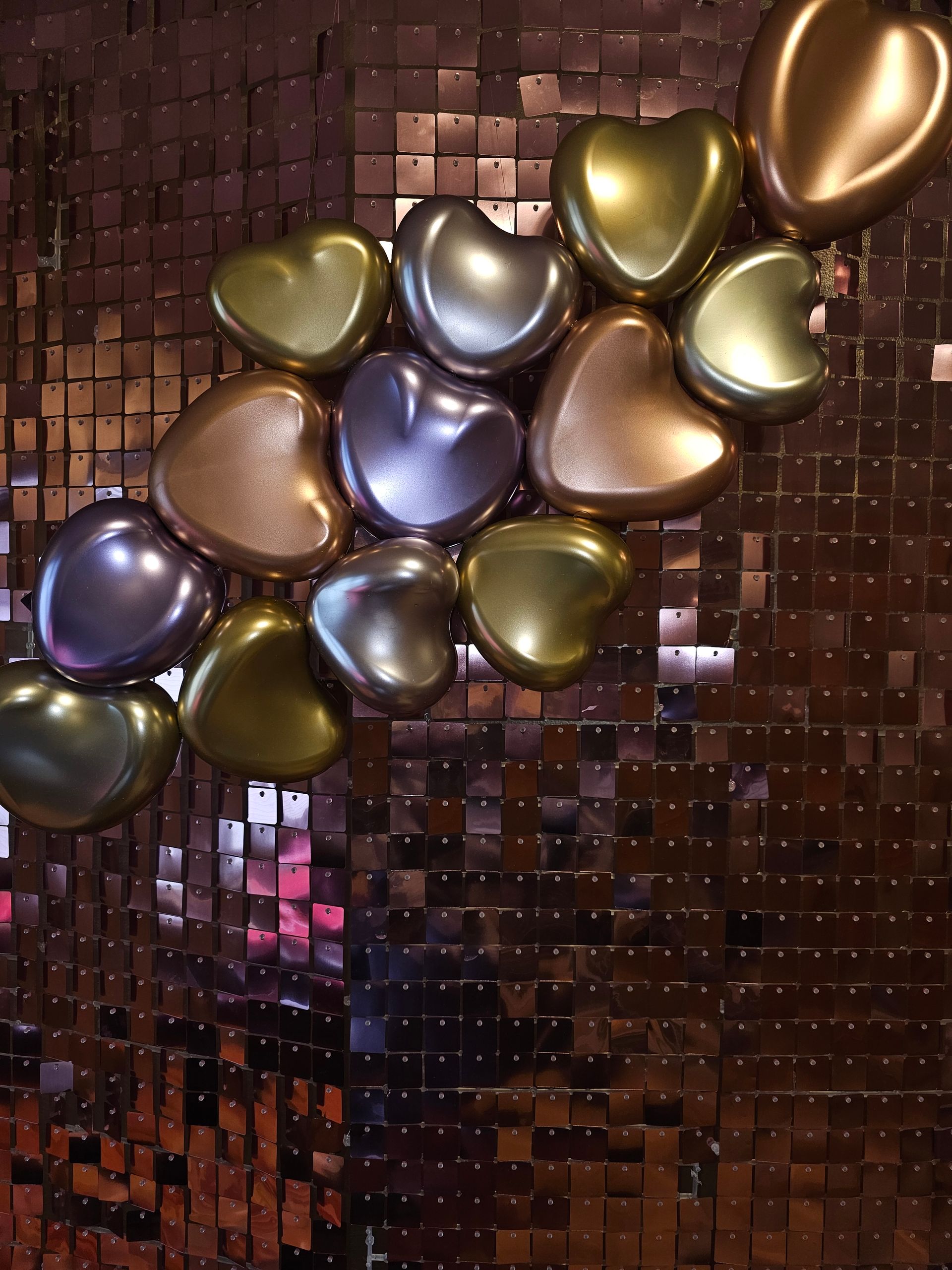 Heart-shaped balloons in metallic colors against a bronze sequined wall.