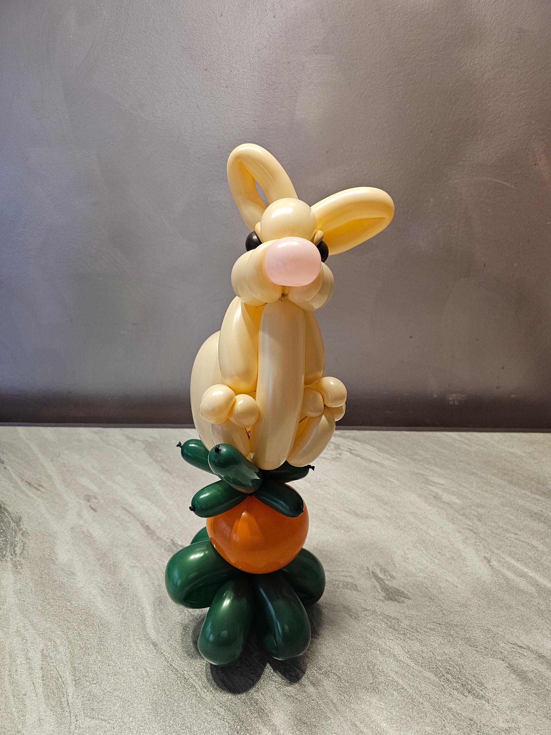 Balloon bunny sculpture on top of a balloon carrot with green leaves.