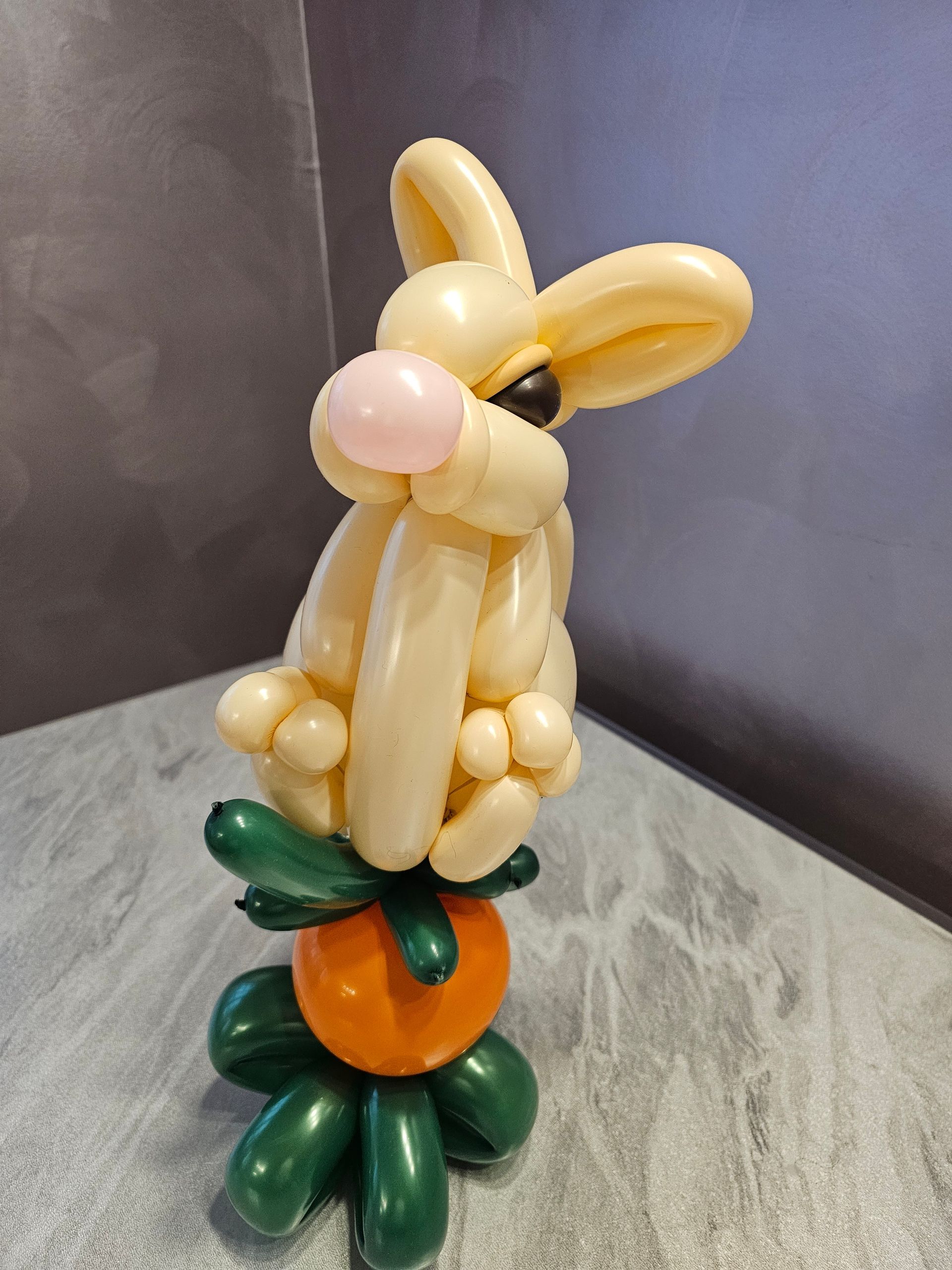 Balloon bunny on an orange balloon carrot. Tan bunny, pink nose, with green leaves.