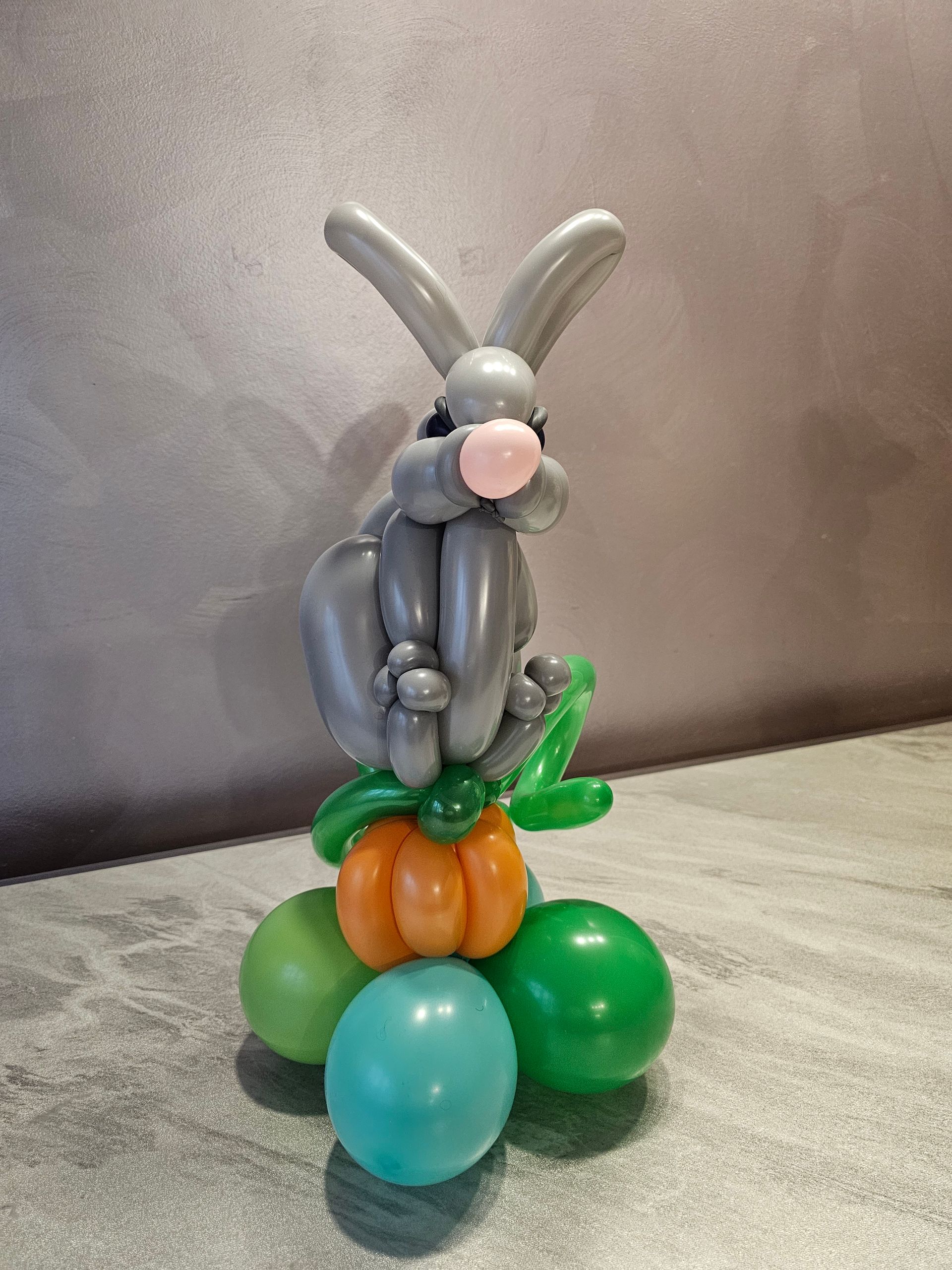 Balloon bunny sculpture with a pumpkin, on green and blue balloons.