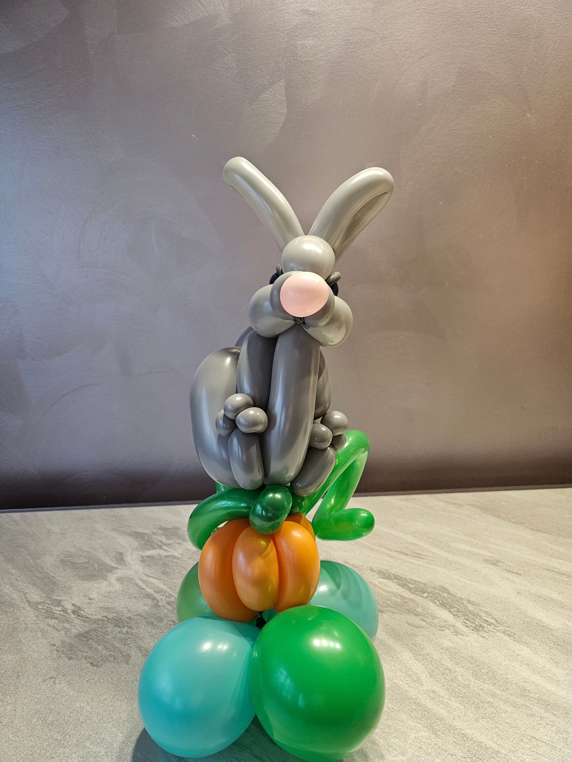 Balloon sculpture of a gray bunny atop a pumpkin and colorful balloons.