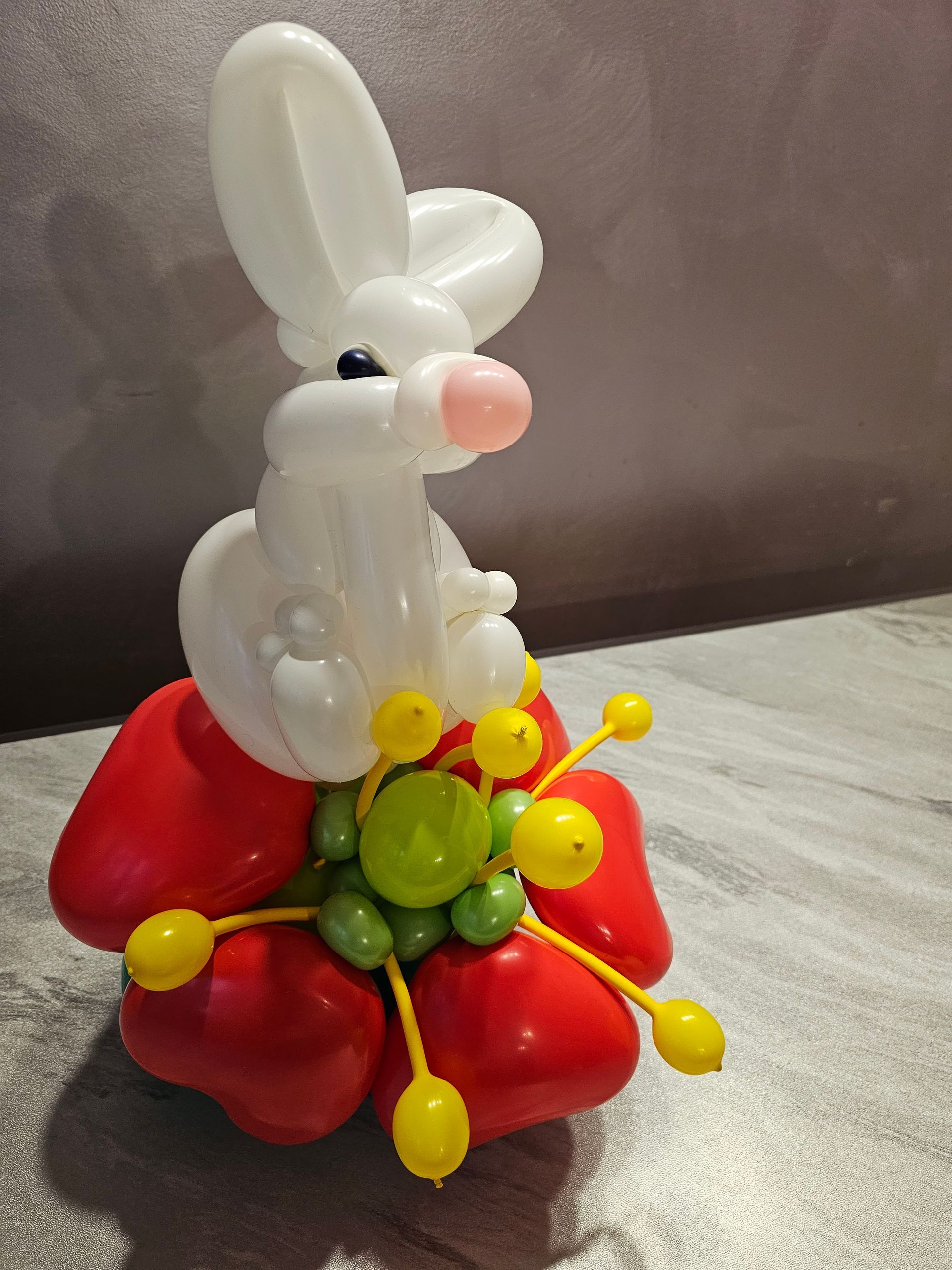 Balloon sculpture of a white bunny with a pink nose, atop a red flower with yellow accents.