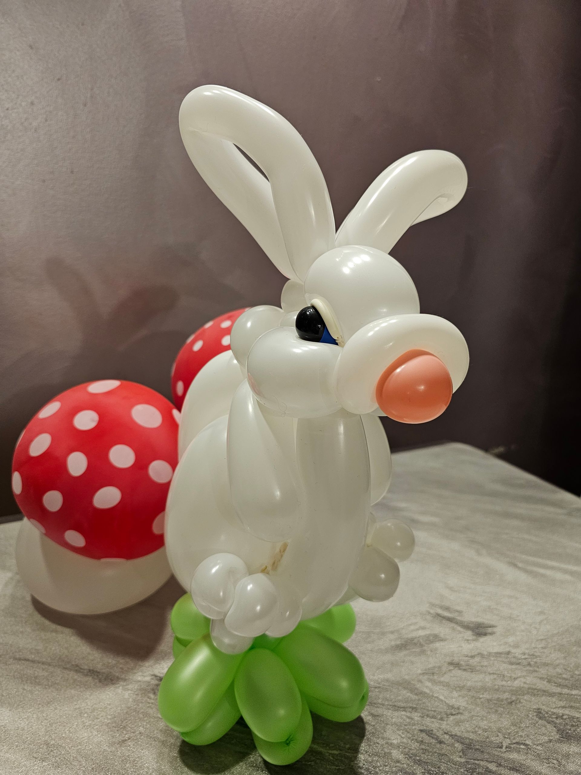 White balloon rabbit with pink nose, blue eyes, and green feet next to a red mushroom balloon with white spots.