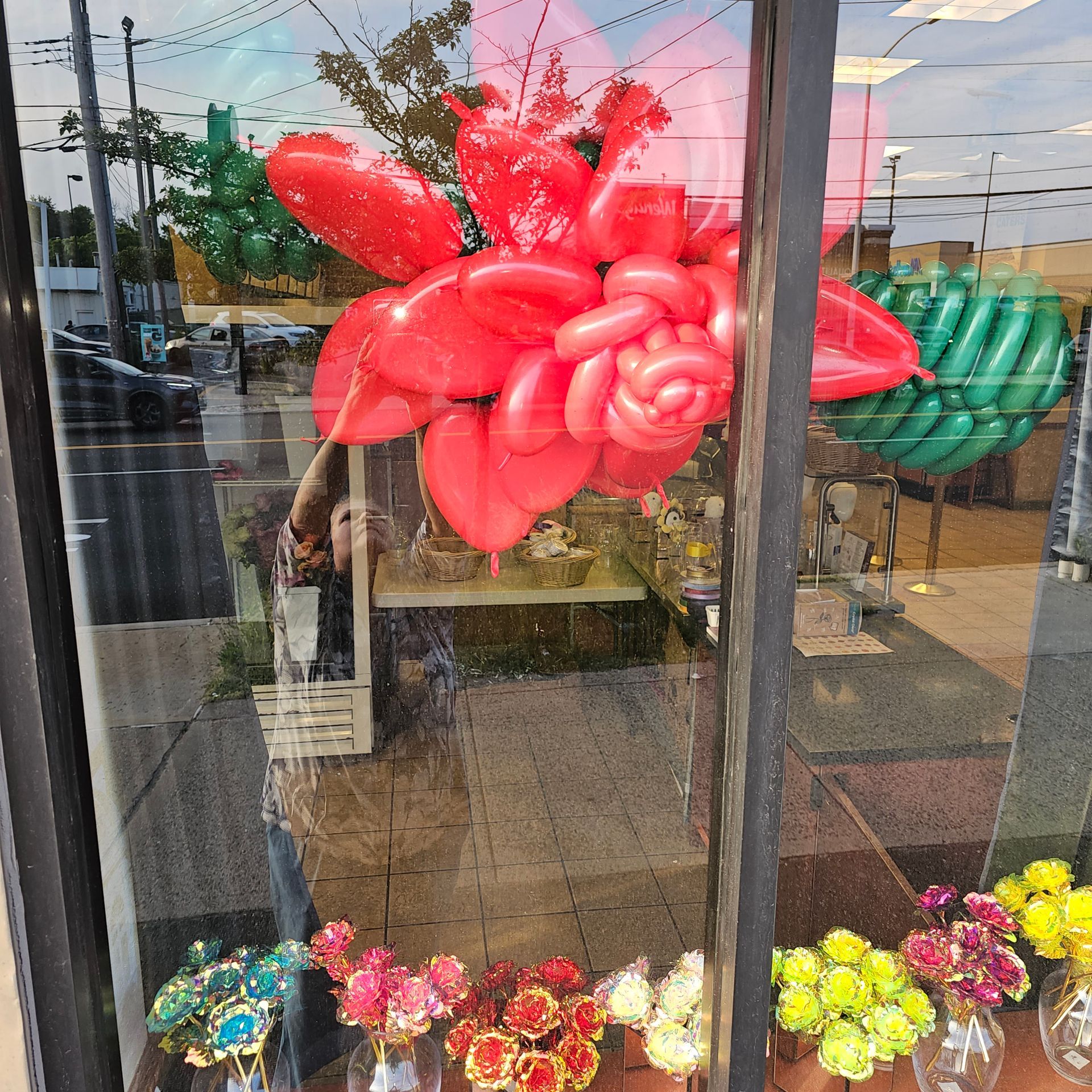 Window display with red balloon art, green balloons, and flowers in vases.