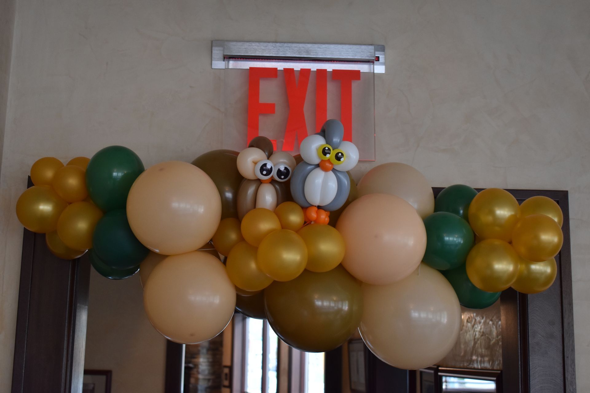 Balloon arch with owl figures above a door with an exit sign.