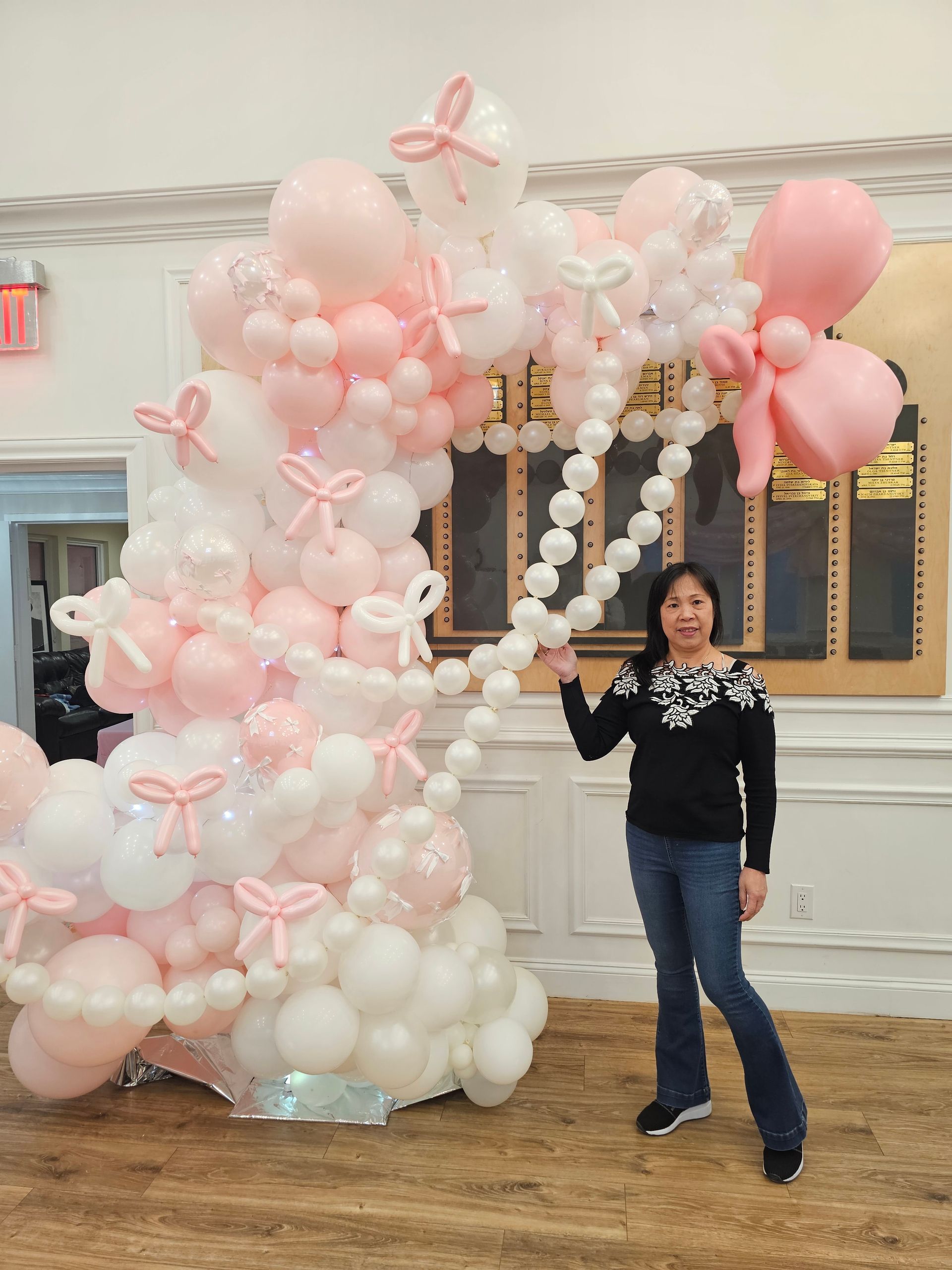 Woman stands next to a large pink and white balloon sculpture decorated with bows.