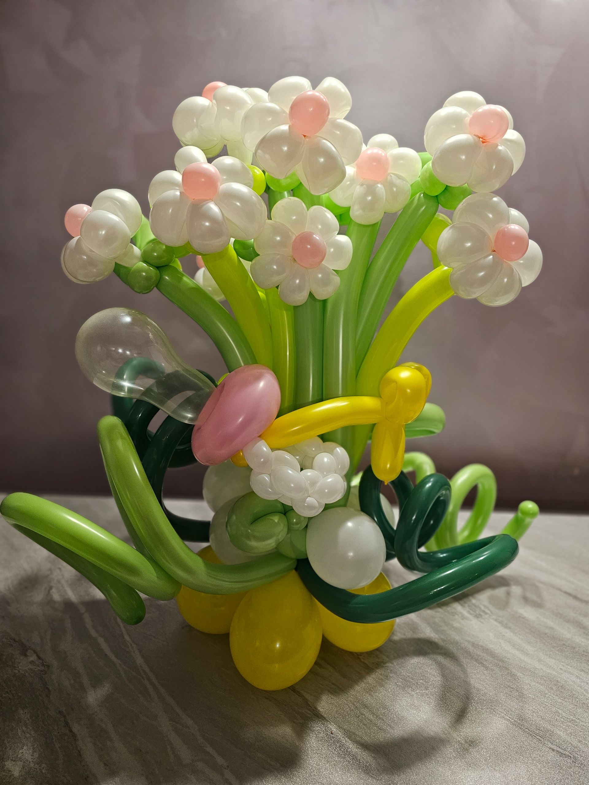Balloon bouquet with white daisies, pink centers, and green stems, set in a yellow base.